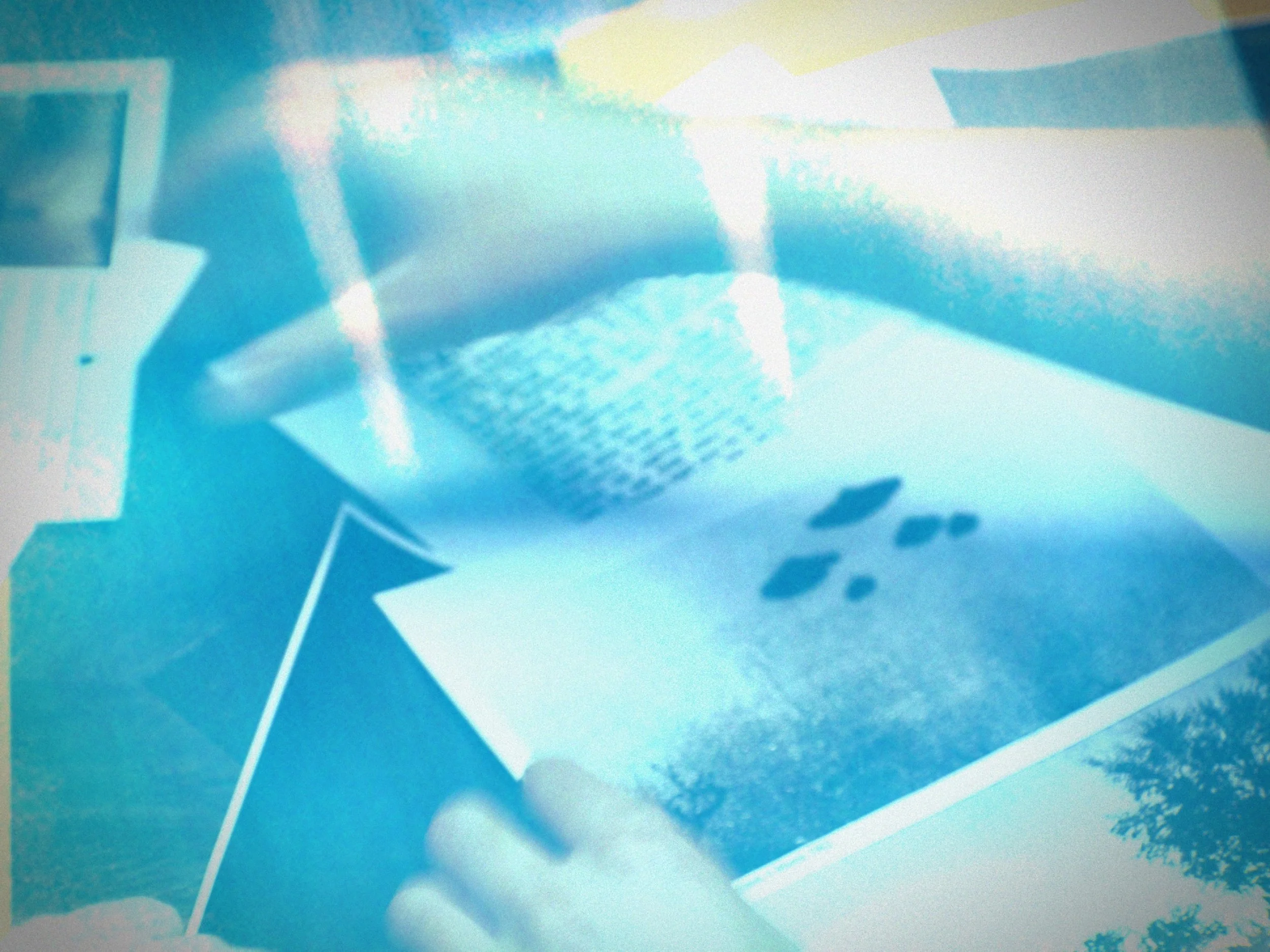 A person holding a pen on a paper with photographs, with a blurred background that includes a landscape and geometric shapes.