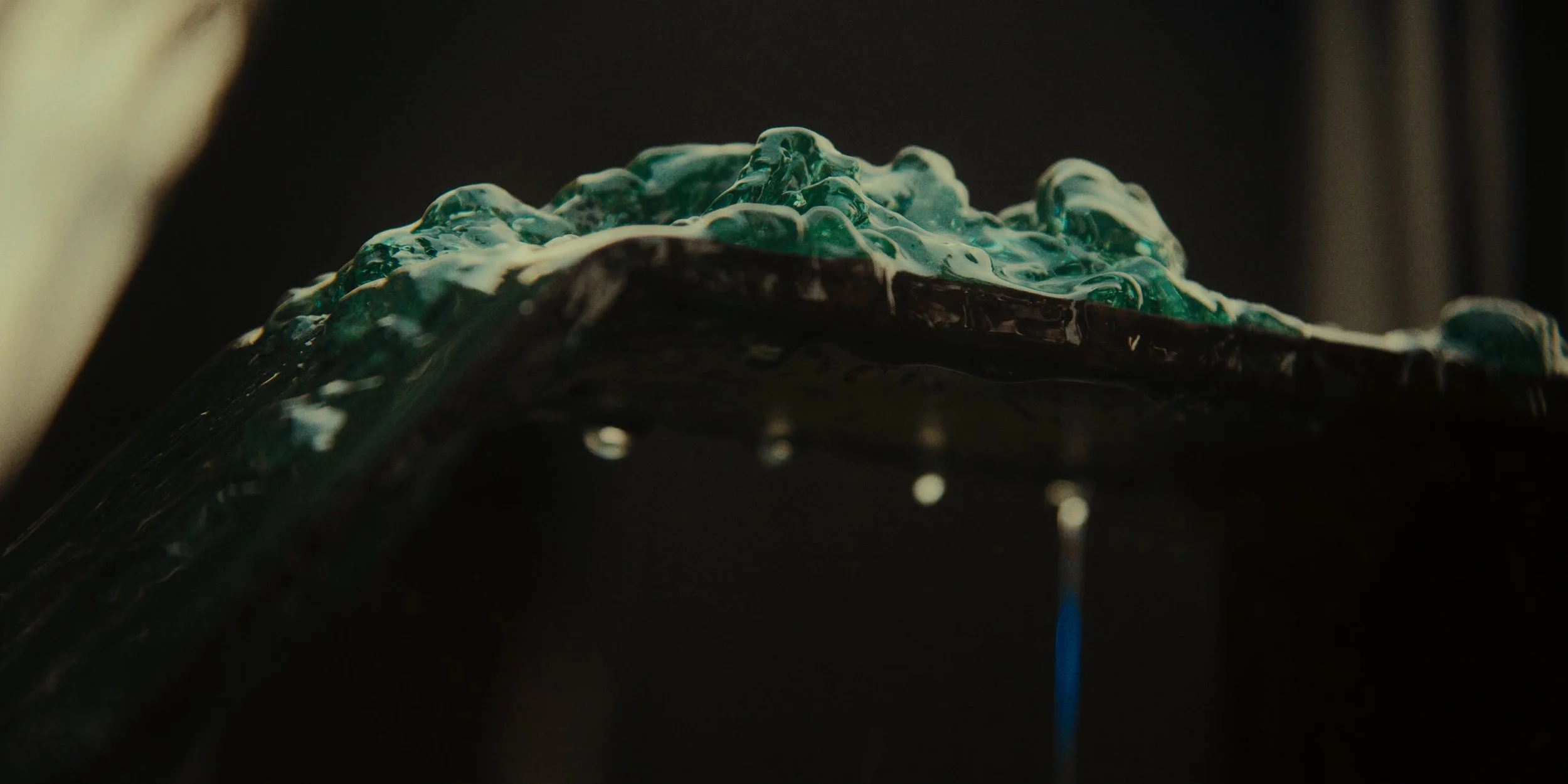 Close-up of a dark, translucent glass art piece with blue-green bubbles and flowing shapes, illuminated in a dim setting.