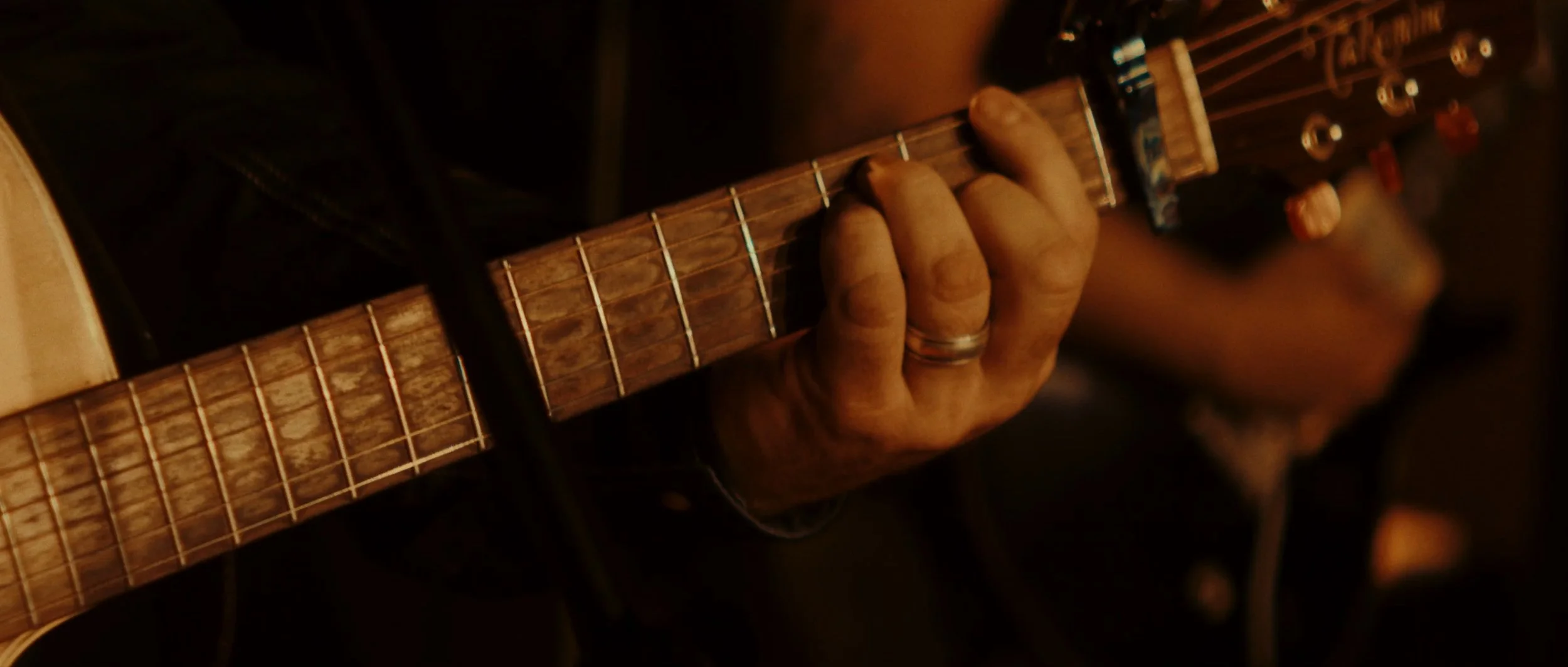 Close-up of a person playing an acoustic guitar, focusing on their hand pressing down on the fretboard.
