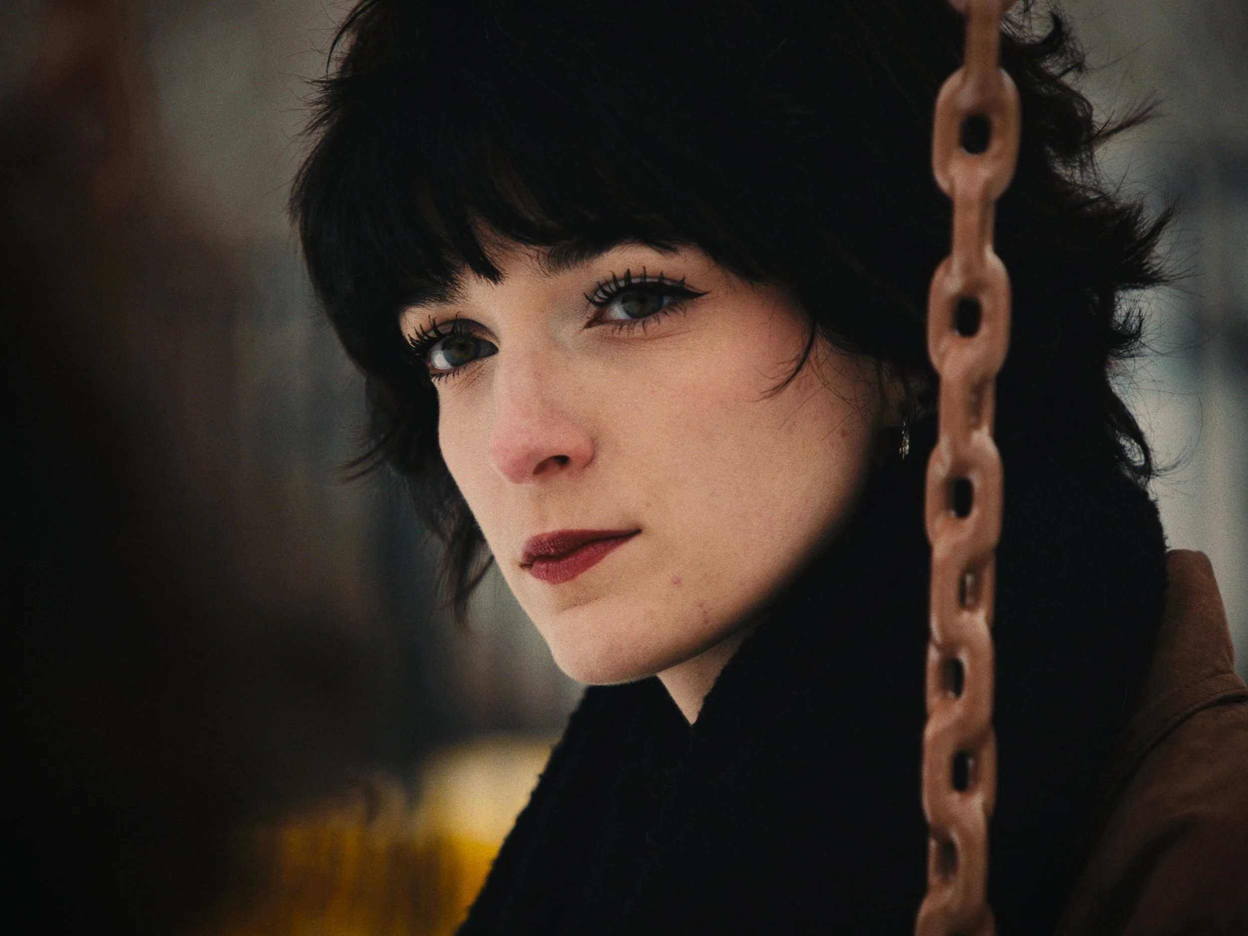Close-up of a woman with short dark in a spotting school with a tan chain in the foreground.
