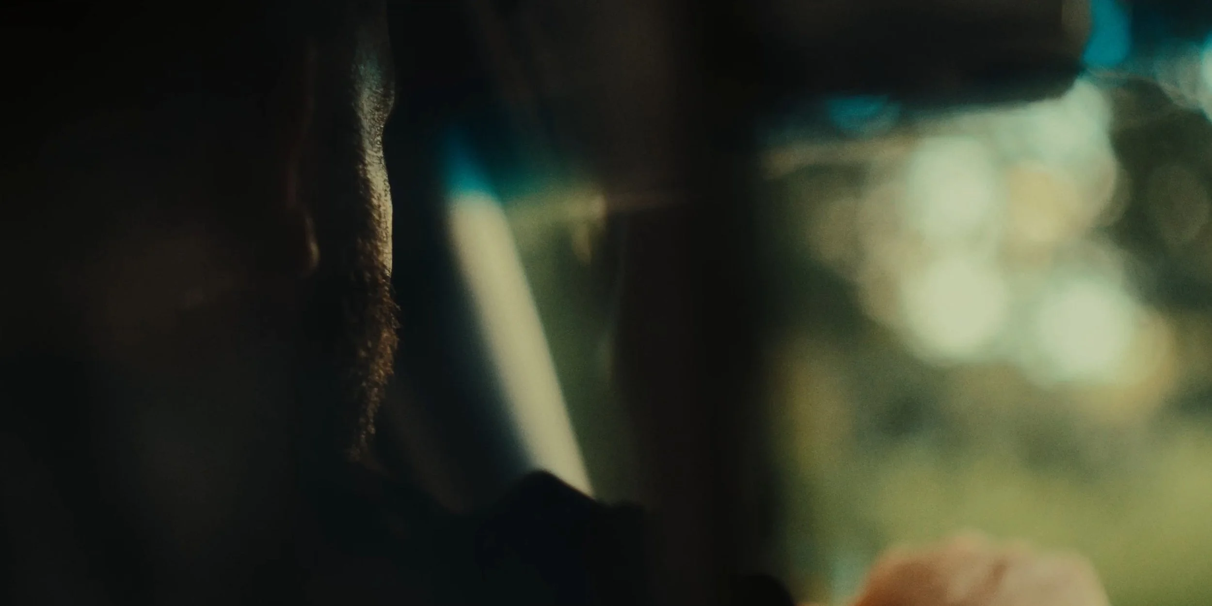 Close-up of a person's face in profile, with a blurred background indicating they are in a vehicle, possibly at night or in low light conditions.