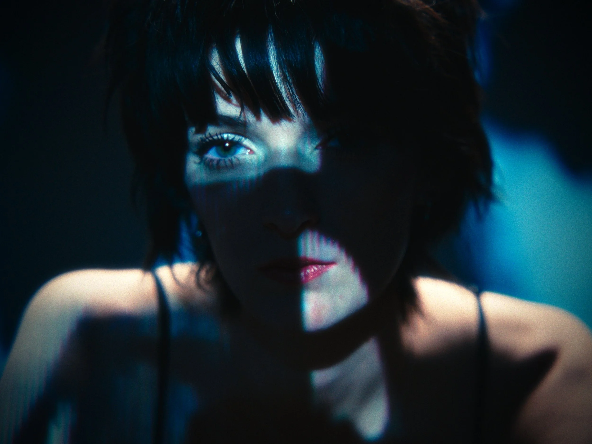 Close-up of a woman's face in low lighting, with one eye illuminated by a blue light, creating shadow effects.