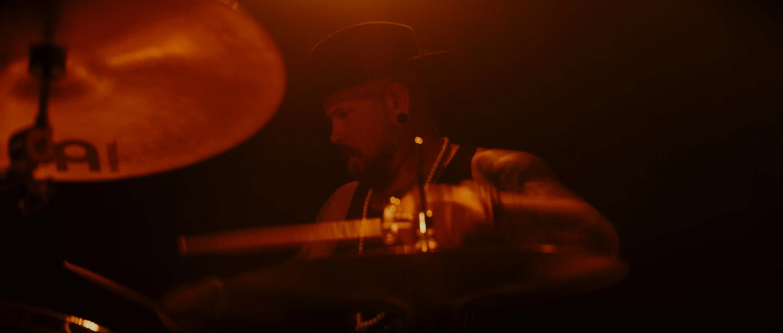 A man playing a drum kit in a dimly lit room with warm, orange lighting.