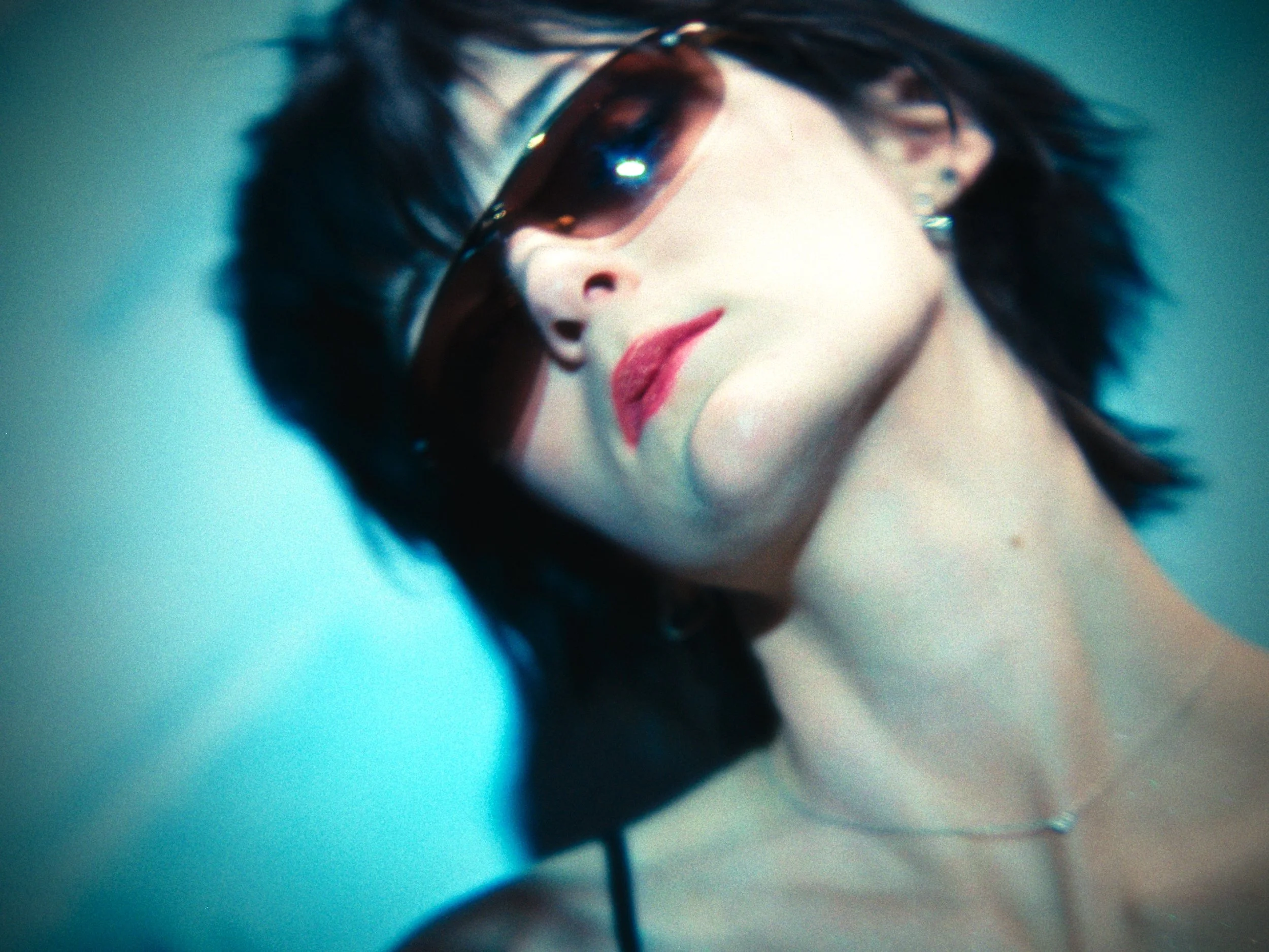 Close-up of a woman with dark hair wearing large sunglasses and red lipstick, resting her head on her hand.