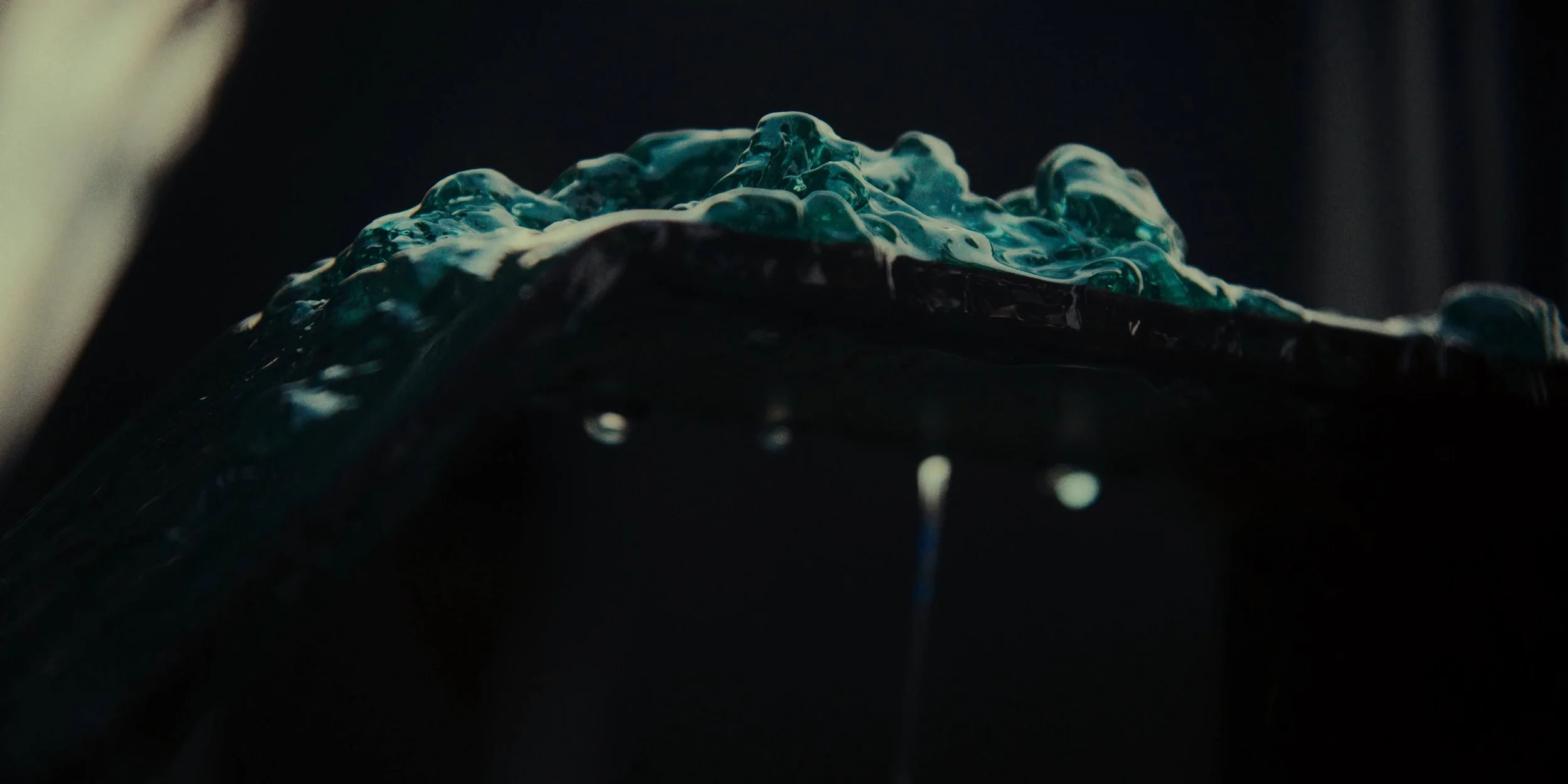 Close-up of a flowing, bubbling blue liquid or gel against a dark background.