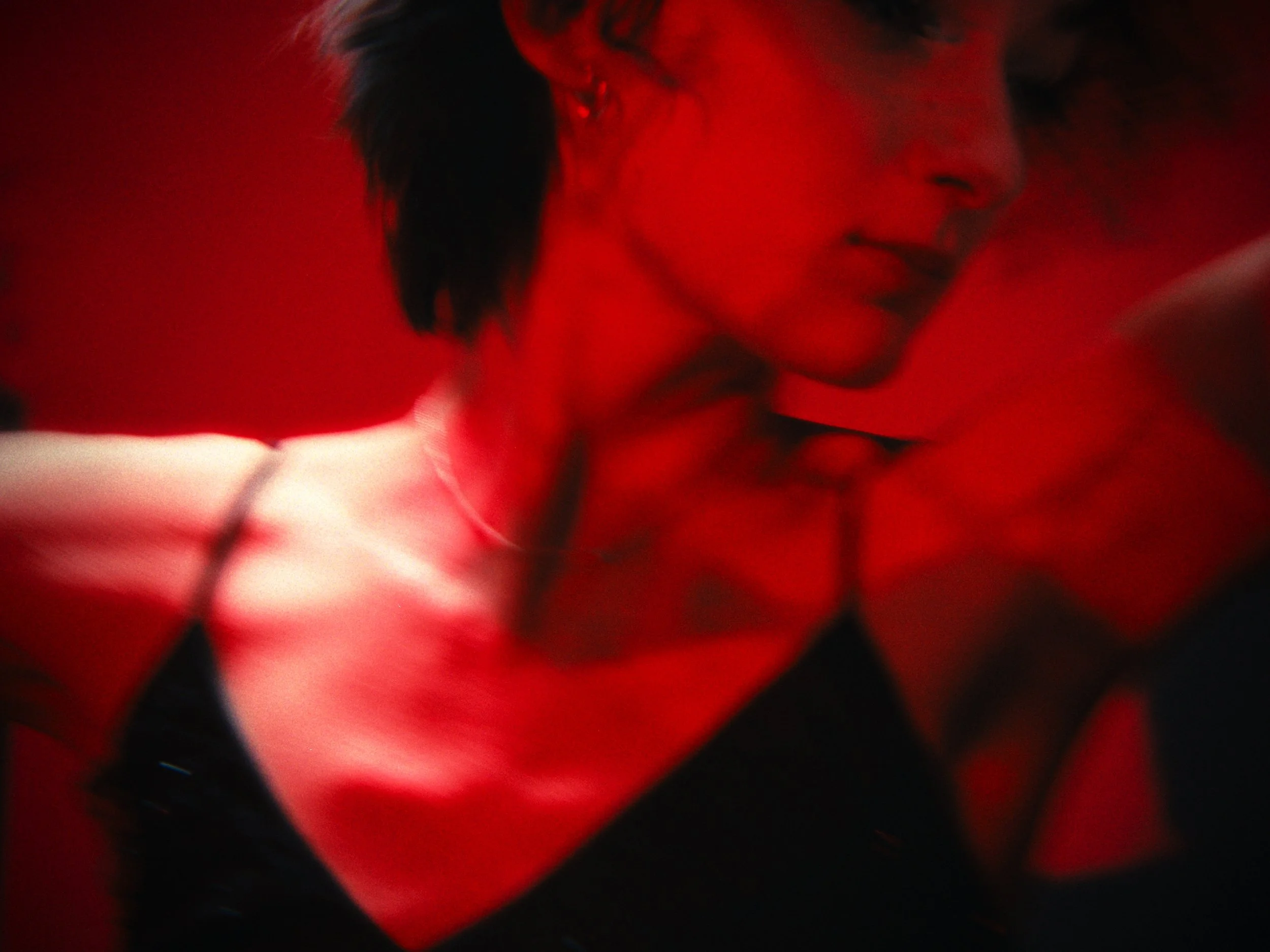 A woman with short dark hair and earrings looking down against a red background.