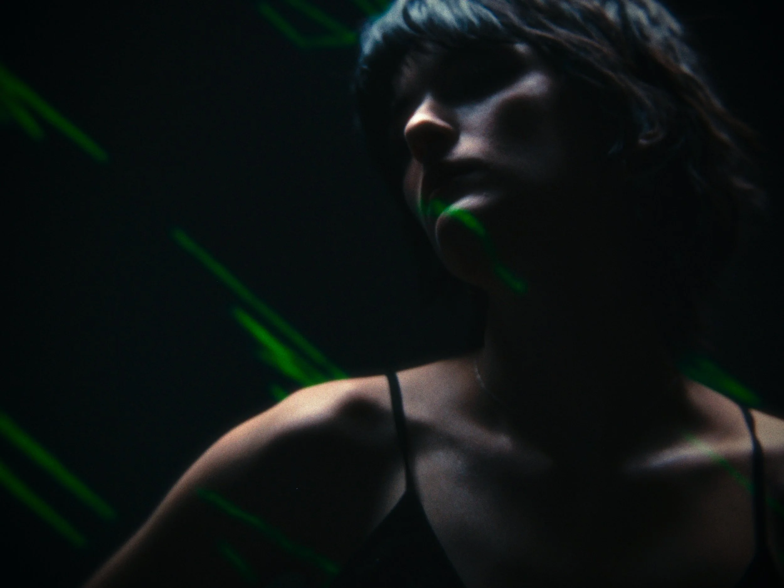 A person with brown hair wearing headphones in a dark room with green laser lights.