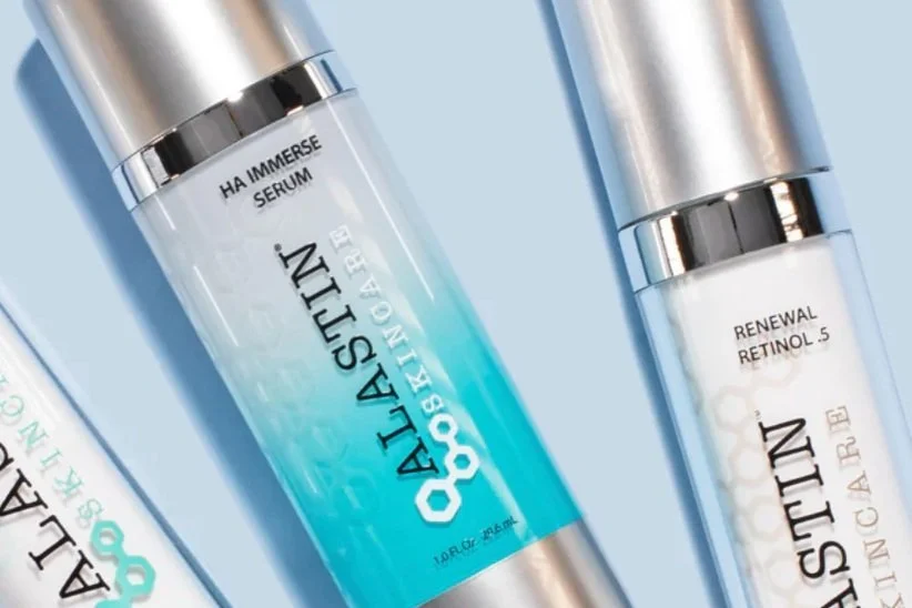 Two skincare serum bottles with silver caps, one labeled 'HA Immense Serum' and the other 'Renewal Retinol .5', set against a light blue background