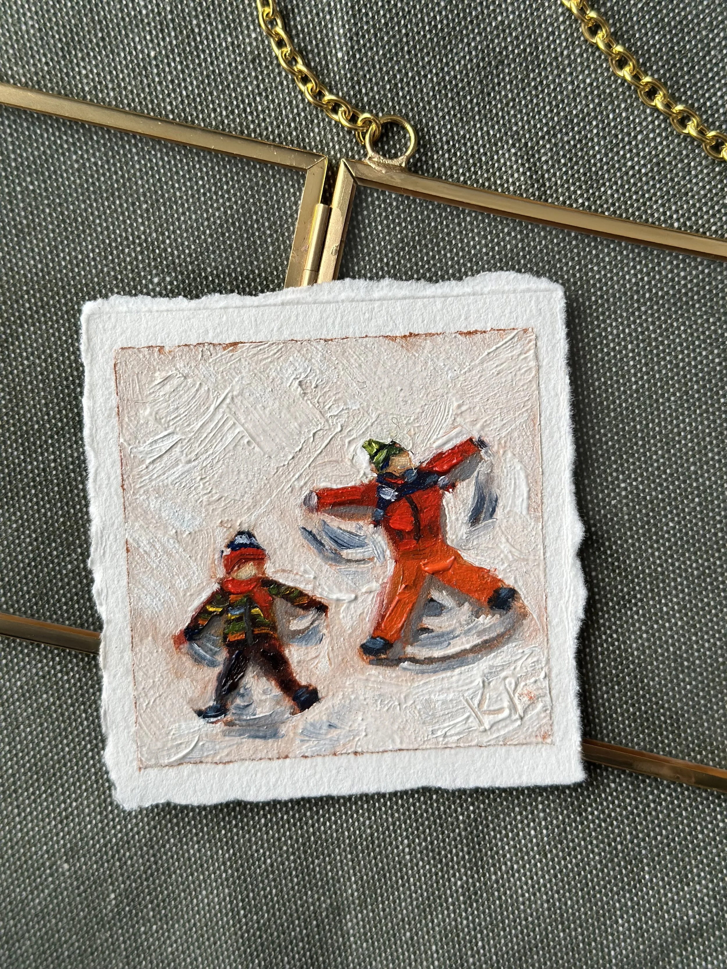 A small textured painting of two children ice skating, one larger and one smaller, with the larger wearing an orange winter coat and the smaller in a dark coat with colorful stripes, set on a gray textured background with a gold chain and frame nearb