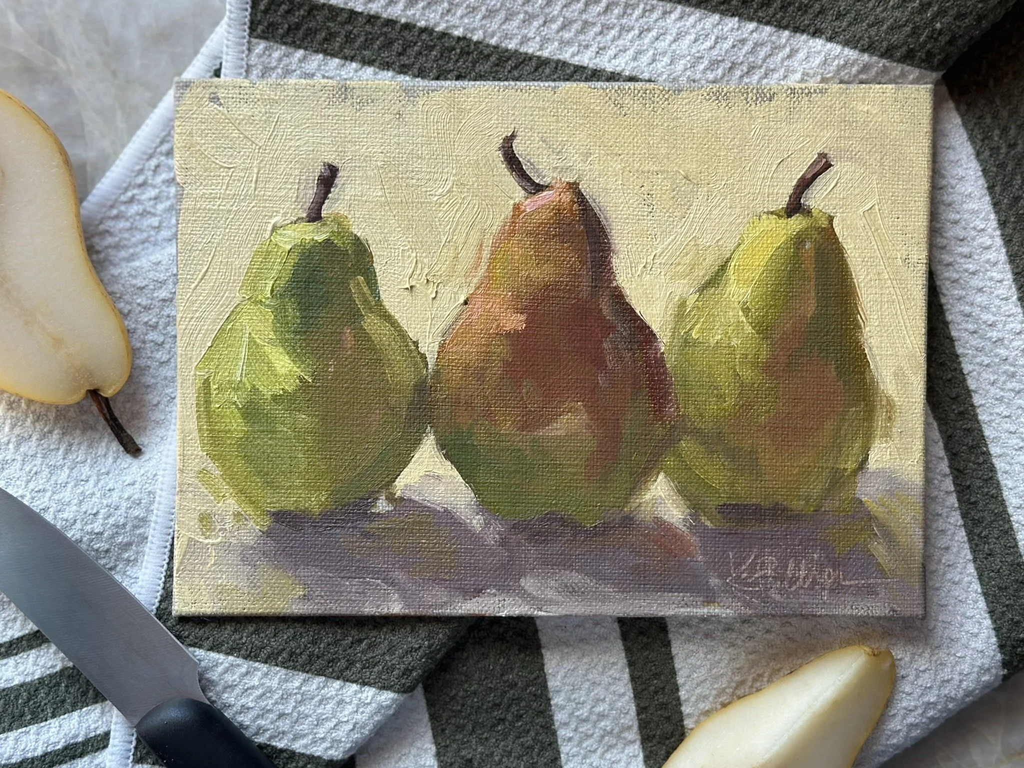 A small oil painting of three pears, with two green pears on the sides and a larger red and green pear in the center, set on a textured surface.