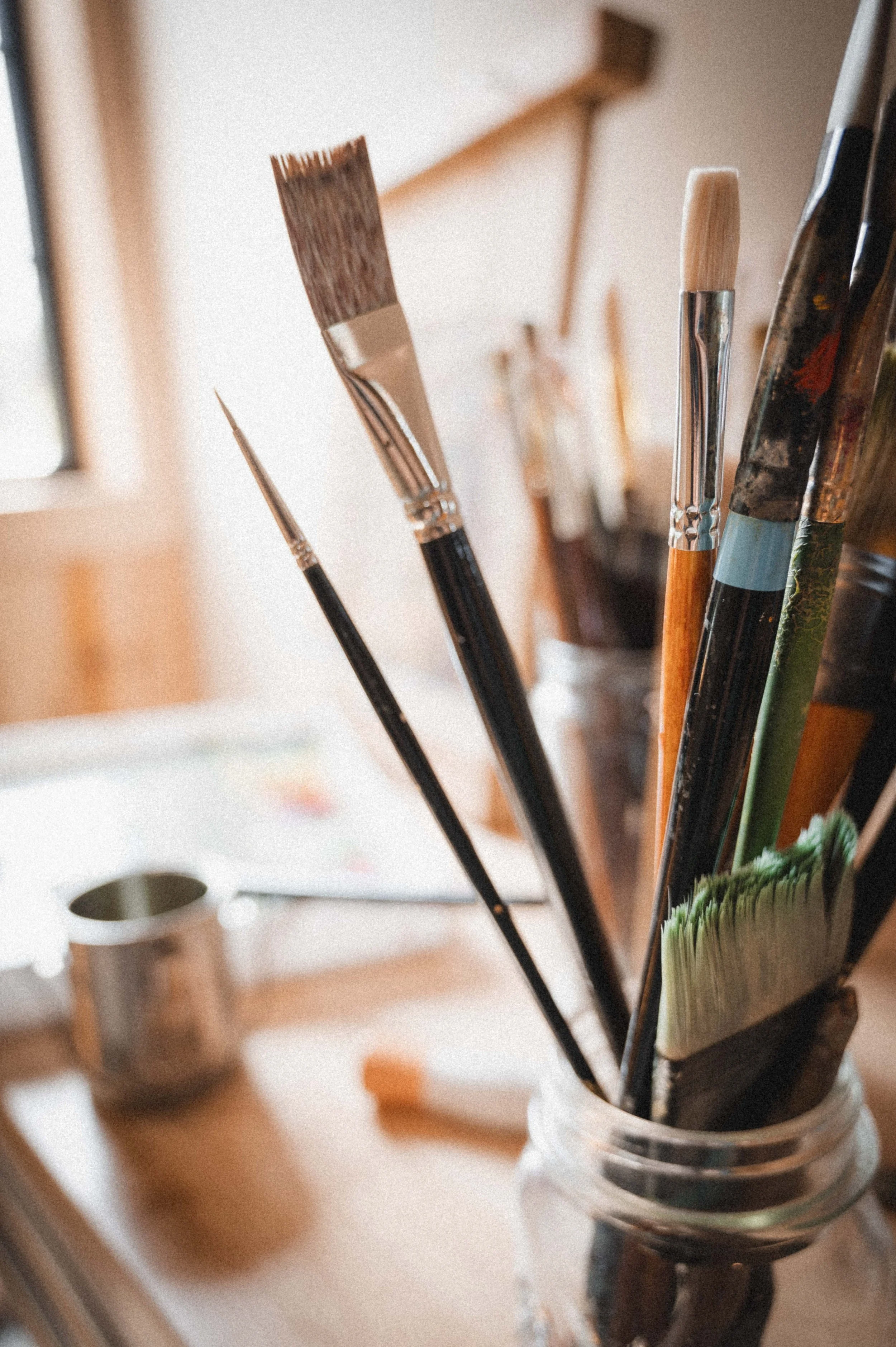A jar containing various paintbrushes on a wooden surface in an art studio.