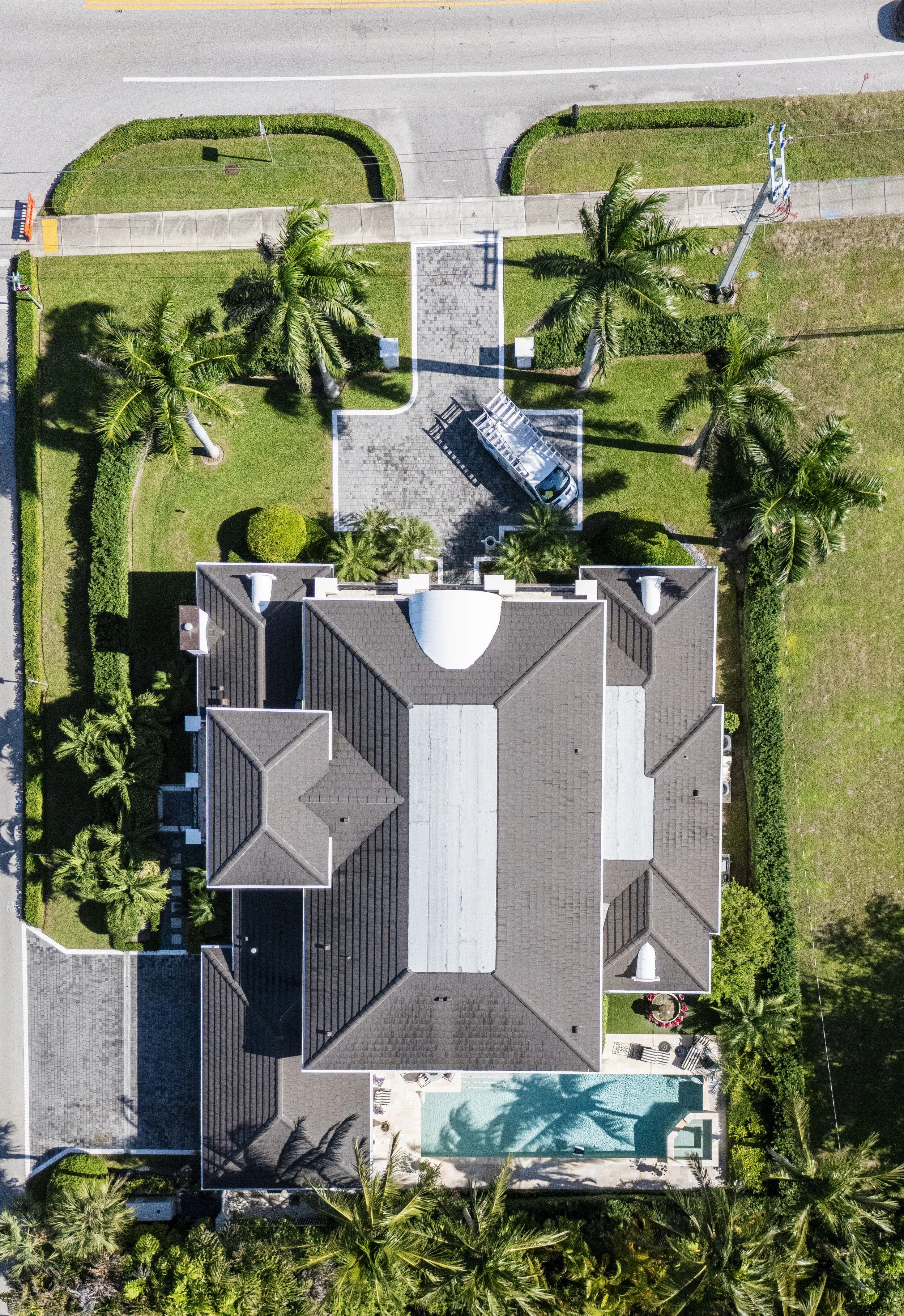 Aerial view of a house with a backyard, swimming pool, palm trees, well-maintained lawn, and surrounding greenery.