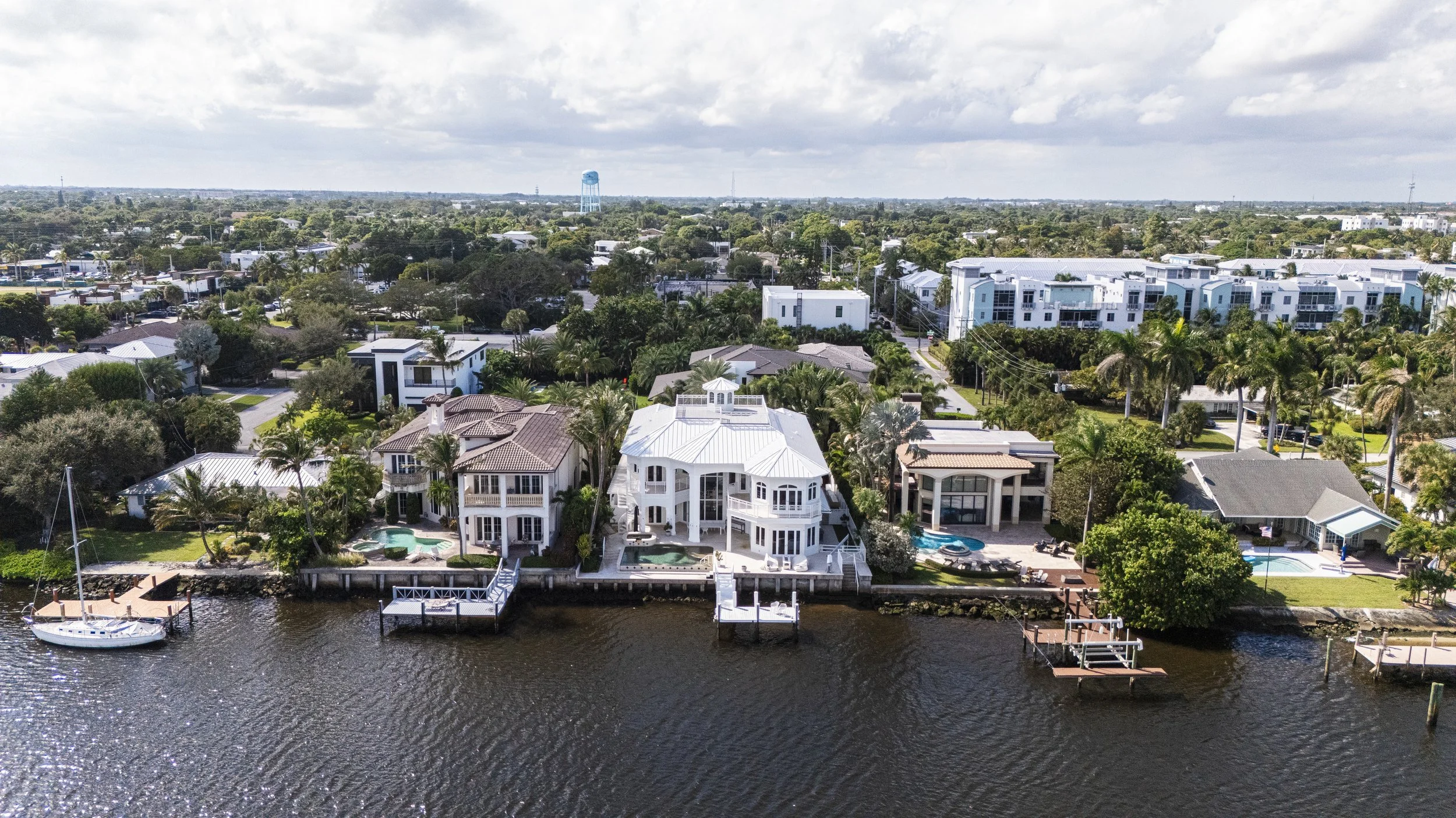 Aerial view of waterfront houses with docks and boats on a river, surrounded by lush trees and lush greenery, in a suburban neighborhood.