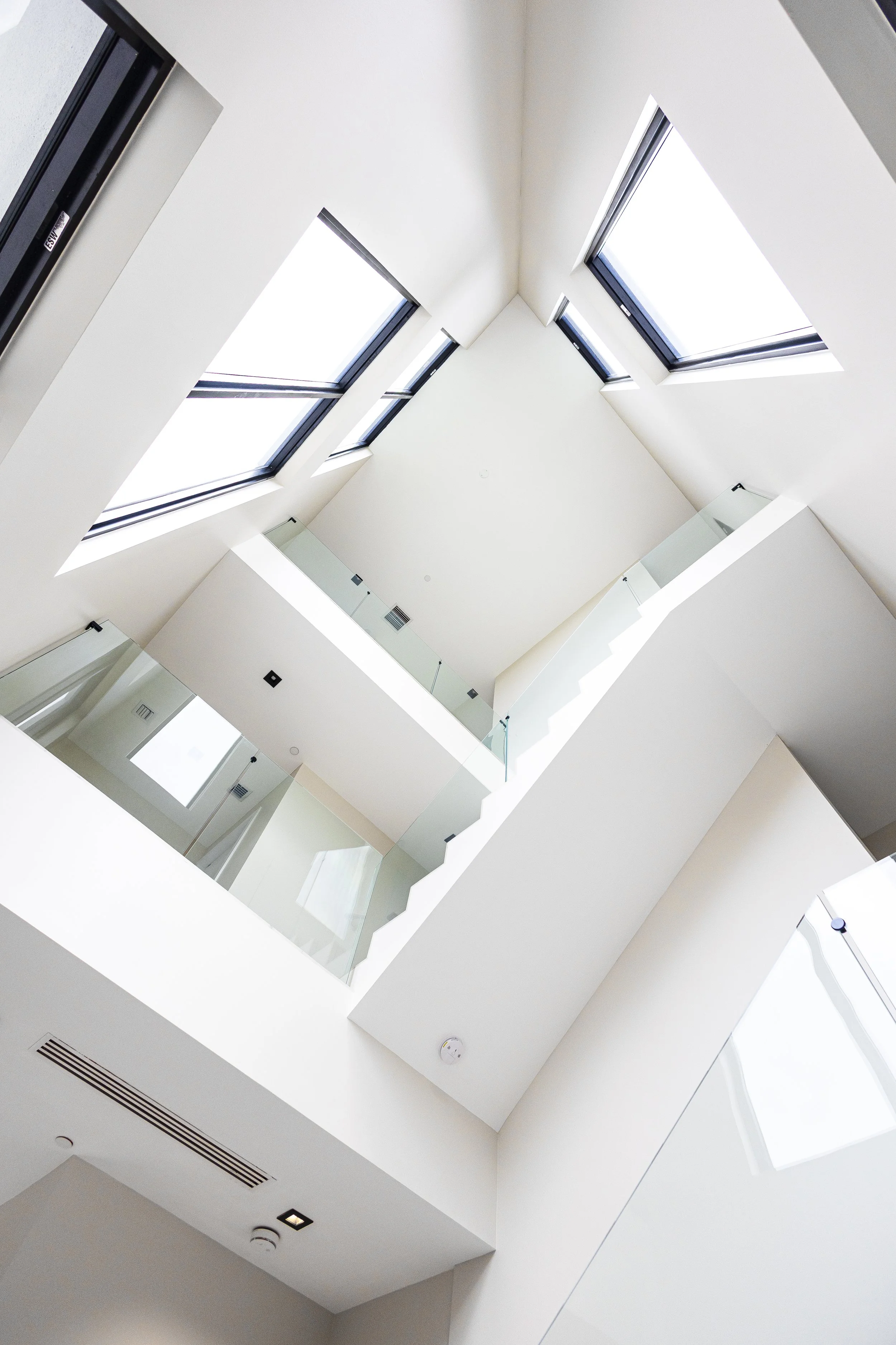 Looking up at a modern atrium with white walls, large skylight windows, and glass railings.