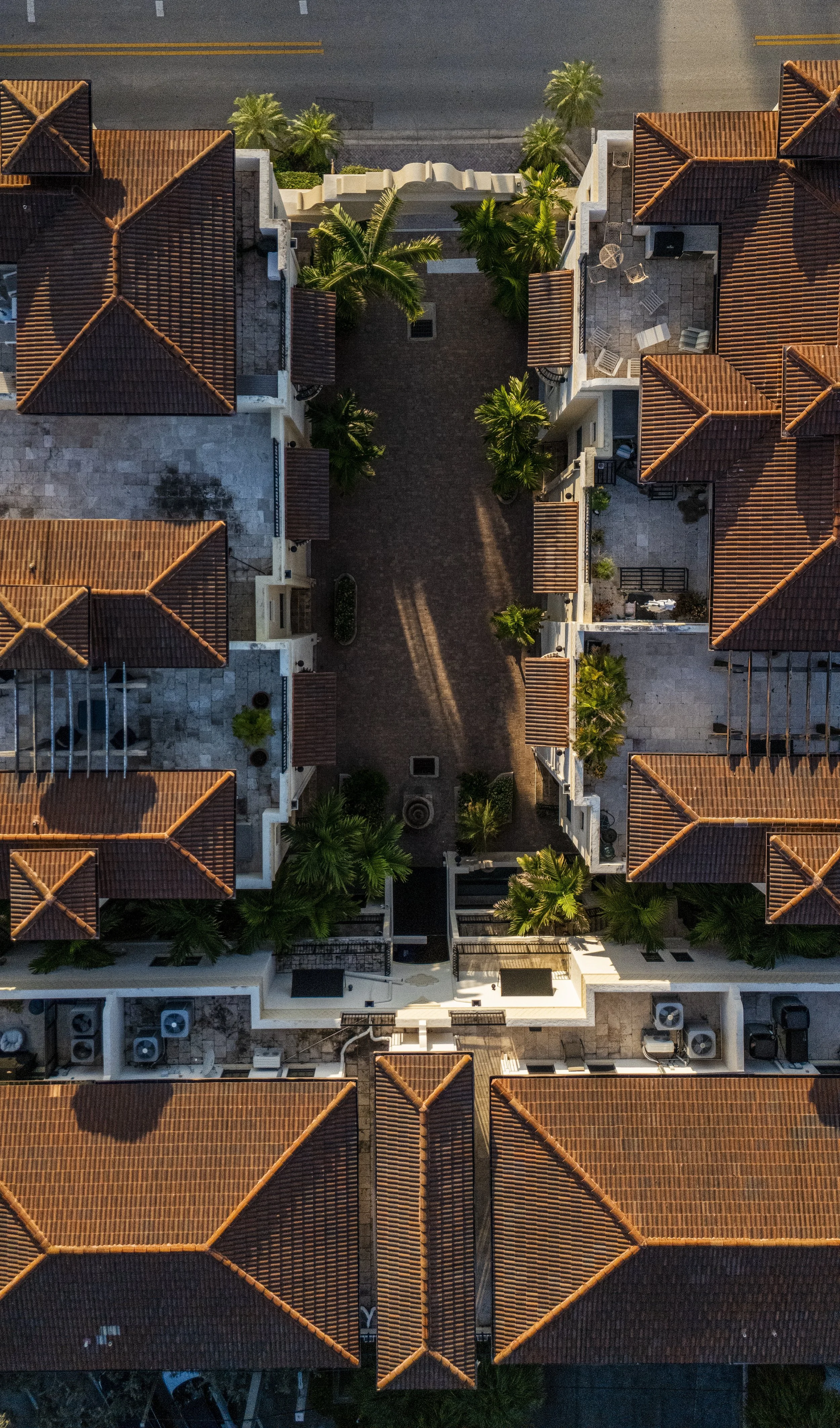 Bird's eye view of a residential complex with red-tiled roofs, palm trees, and a paved courtyard walkway.