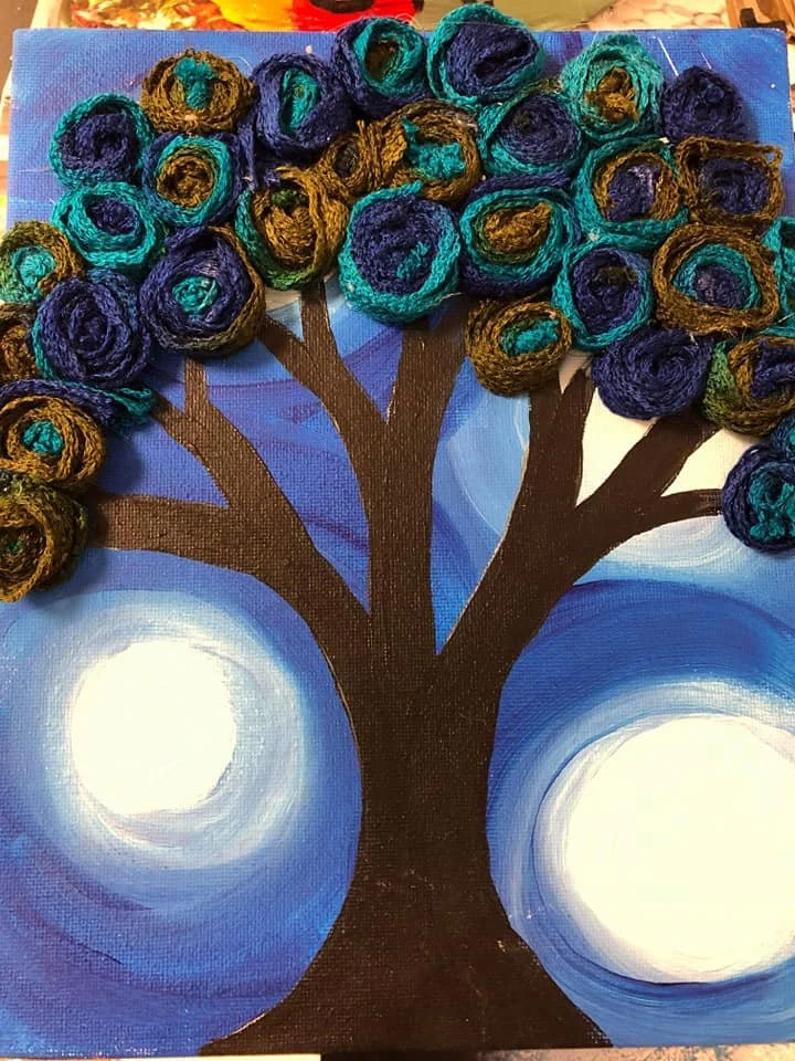 A mixed media artwork featuring a painted tree with three large, glowing orbs in the background and 3D yarn balls forming the tree's canopy.