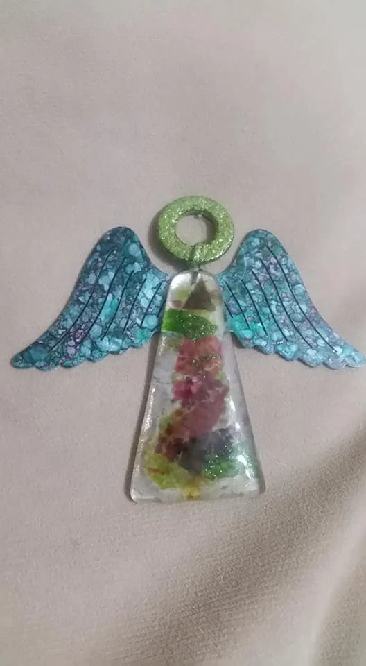 Decorative angel made of a clear resin piece with colorful inside, blue glittery wings, and a green glitter halo on top.