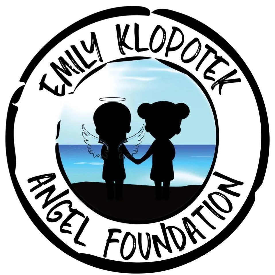 A logo with a central image of two children holding hands on a beach, one with angel wings and a halo, the other with bear ears, against a blue sky and ocean background. Text around the image reads 'Emily Klopek Angel Foundation'.