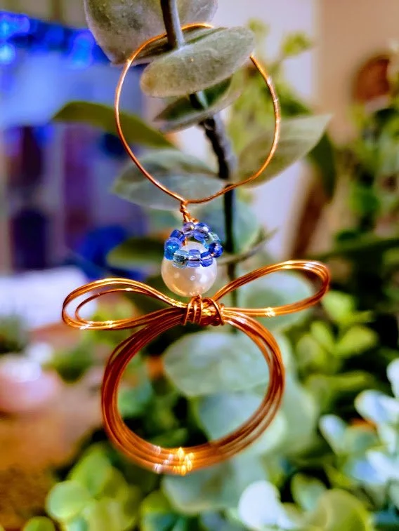 Wire butterfly ornament with a pearl and blue beaded details hanging from a plant.