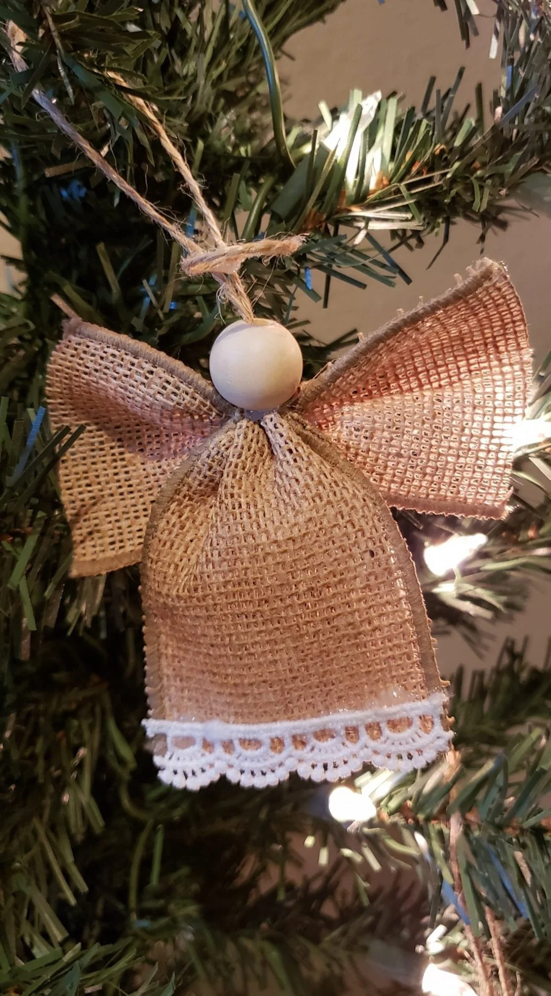 Decorative Christmas ornament on a tree featuring a beige burlap butterfly with white lace trim and a white bead at its center.