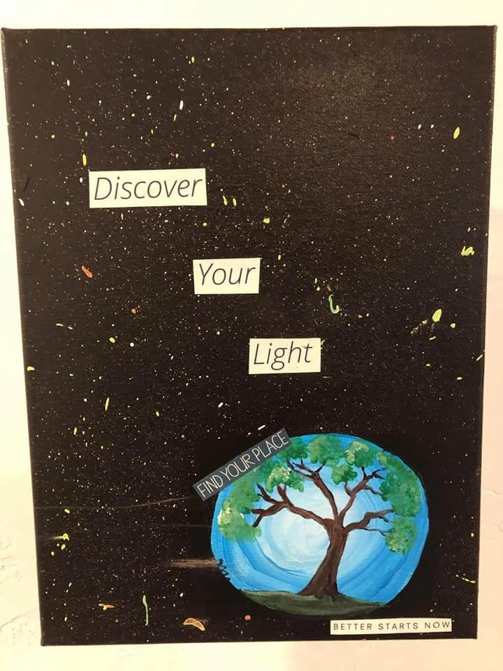 A black poster with a space theme, featuring yellow, white, and red splatters resembling stars. The message reads 'Discover Your Light,' with a painted globe showing a tree on it and text saying 'Find Your Place' and 'Better Starts Now.'