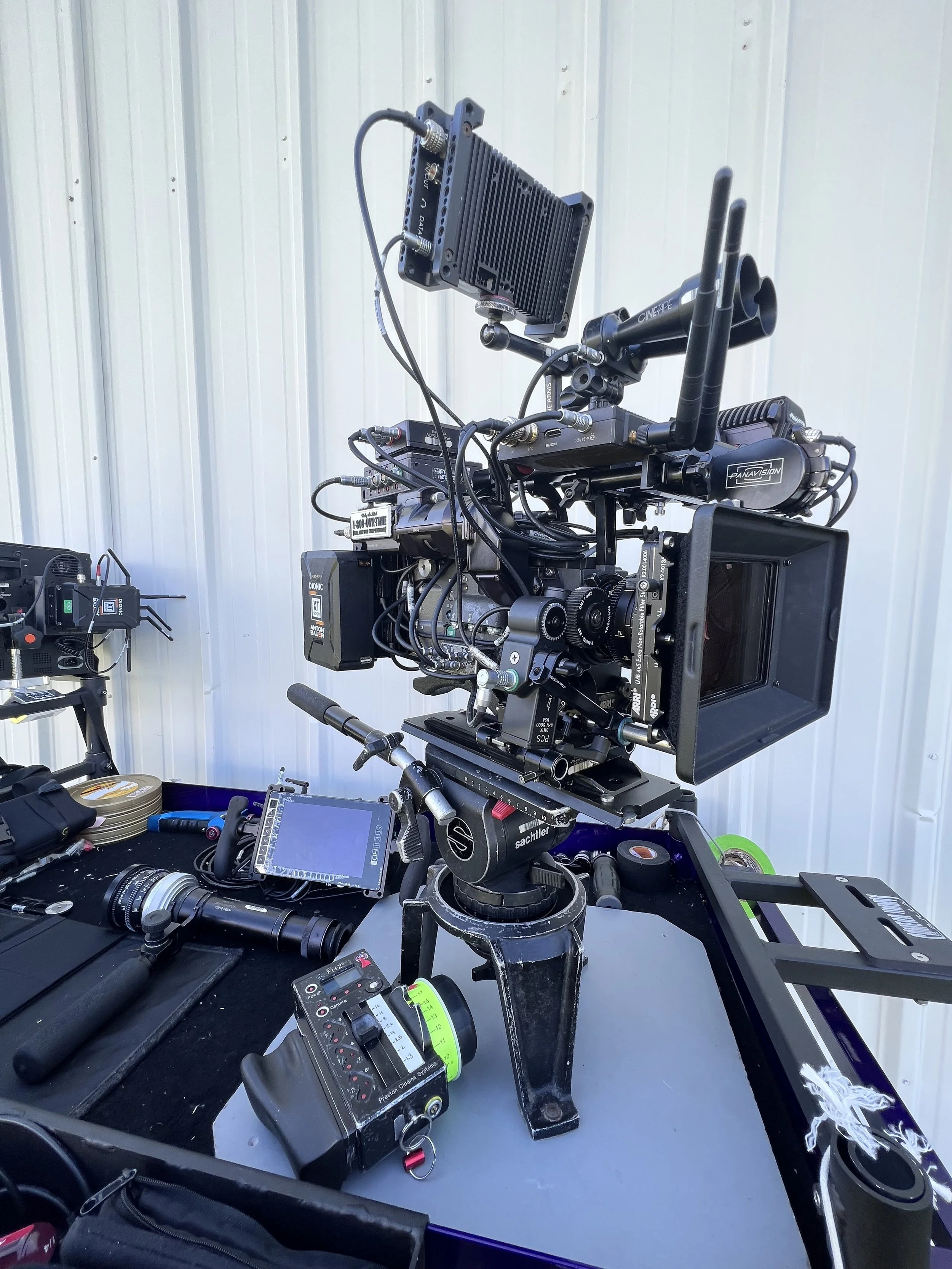 Professional film or video camera setup with various accessories on a table, including a monitor and lens.