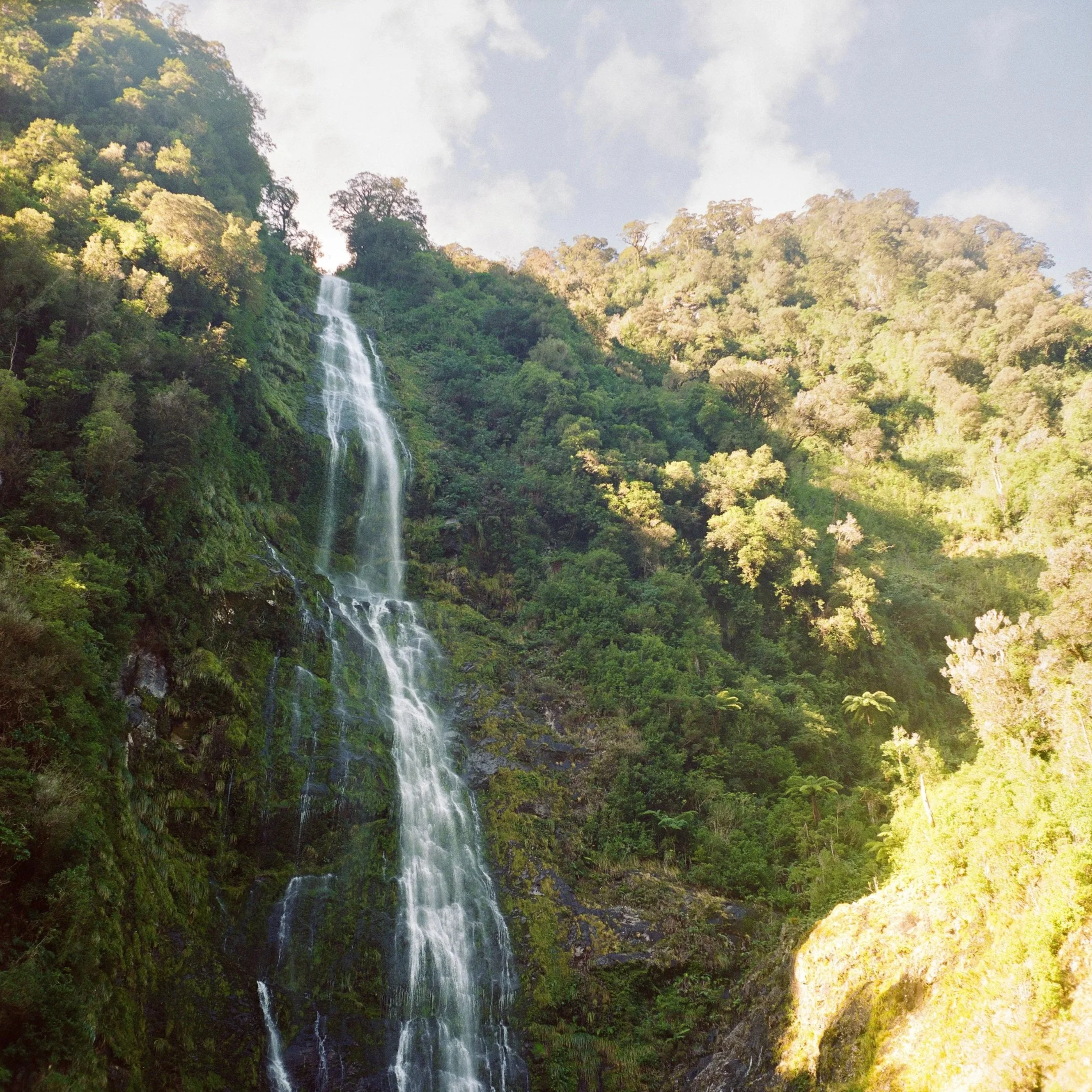 A tall waterfall cascading down a lush green mountainside through trees.