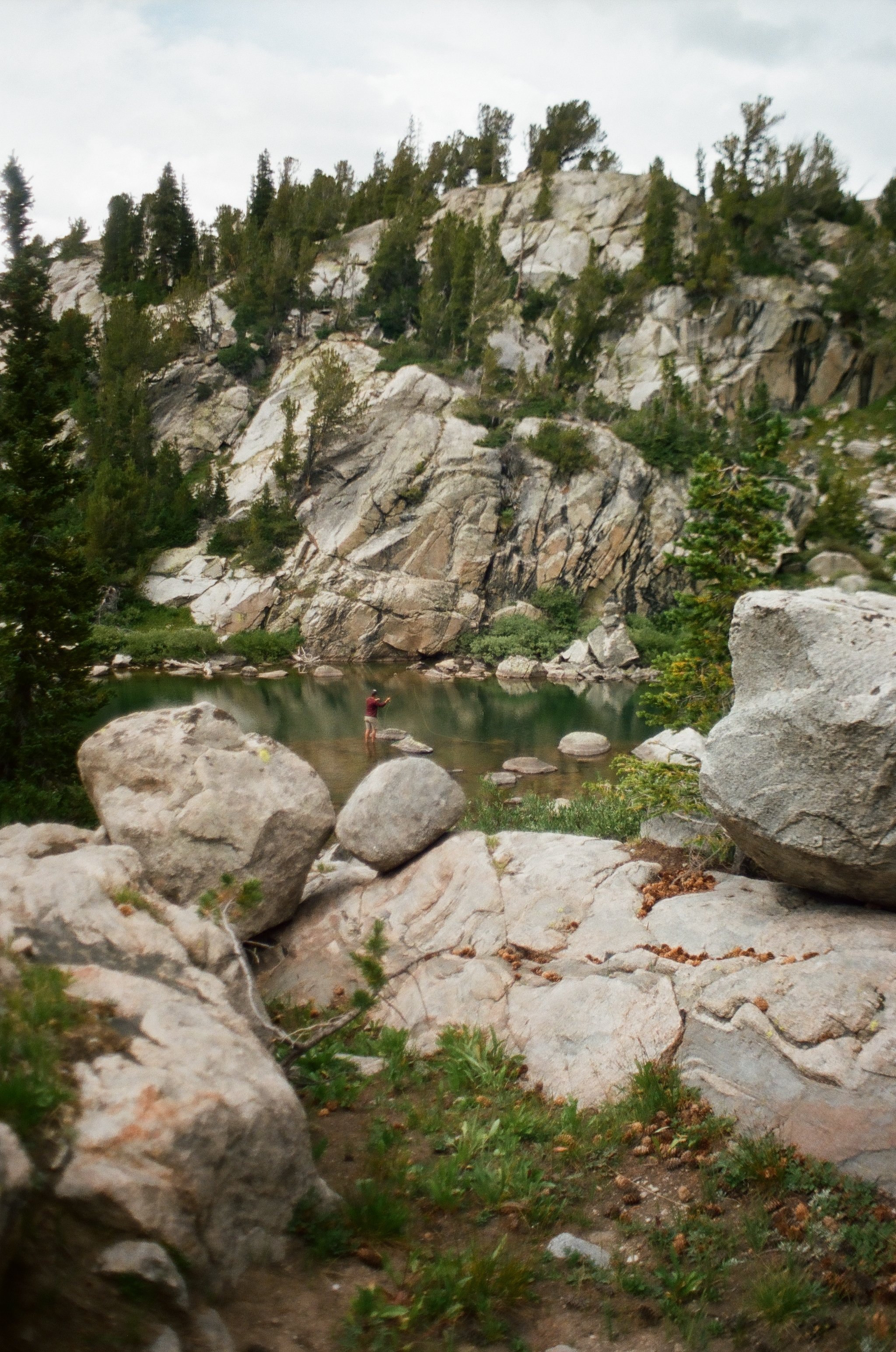 Person standing in water at the base of rocky mountain surrounded by trees.