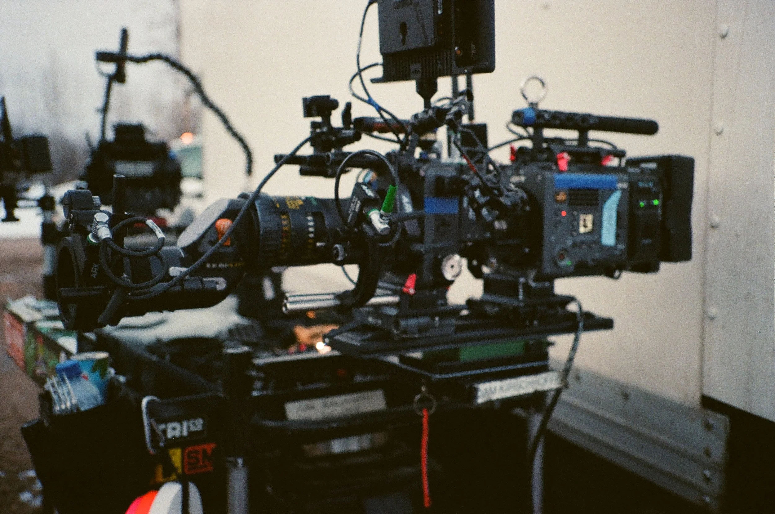 Close-up of a professional film or video camera setup on a tripod, with various lights and accessories in the background.