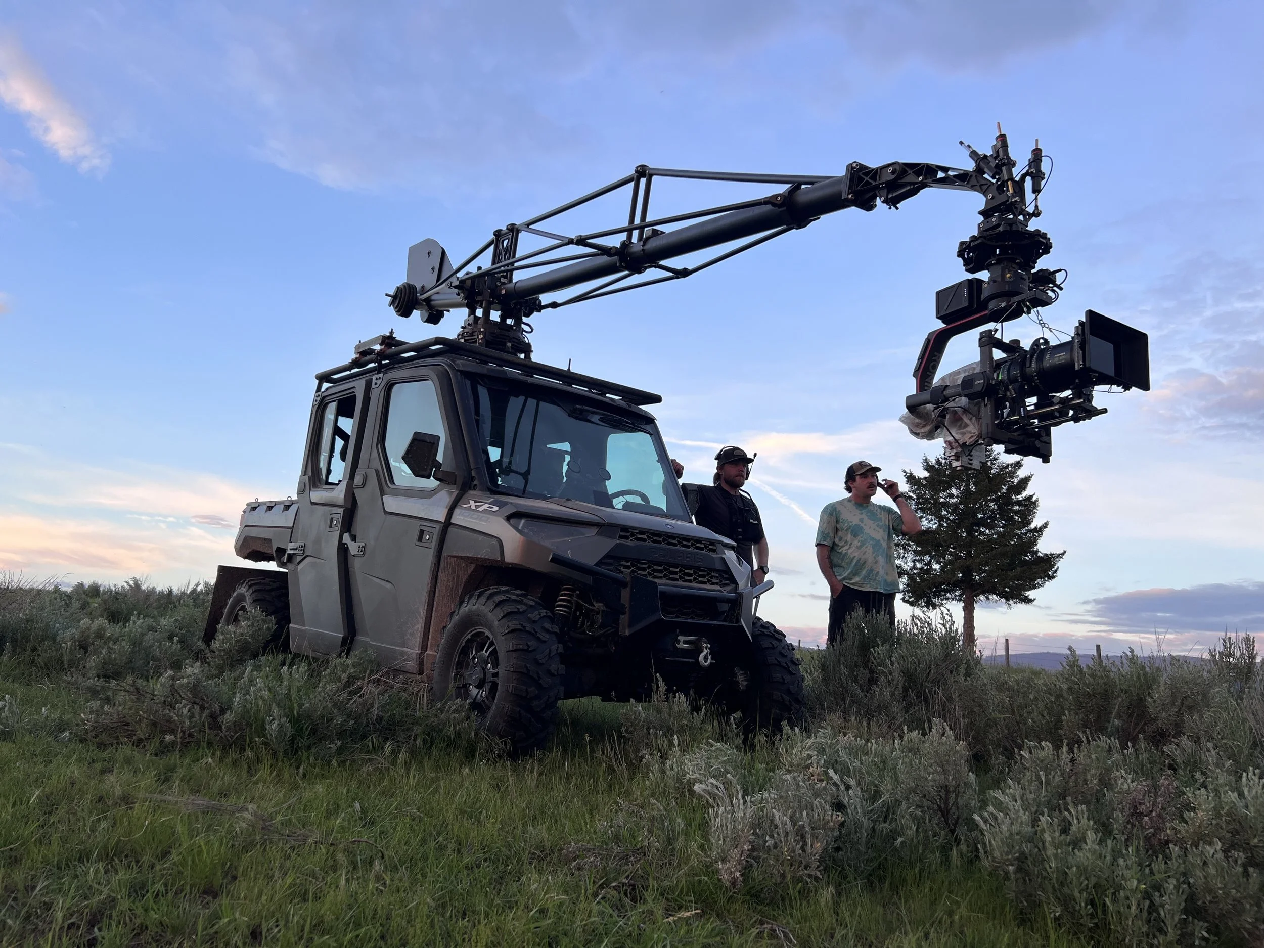 Drone with camera mounted, crew members on grassy field during sunset.