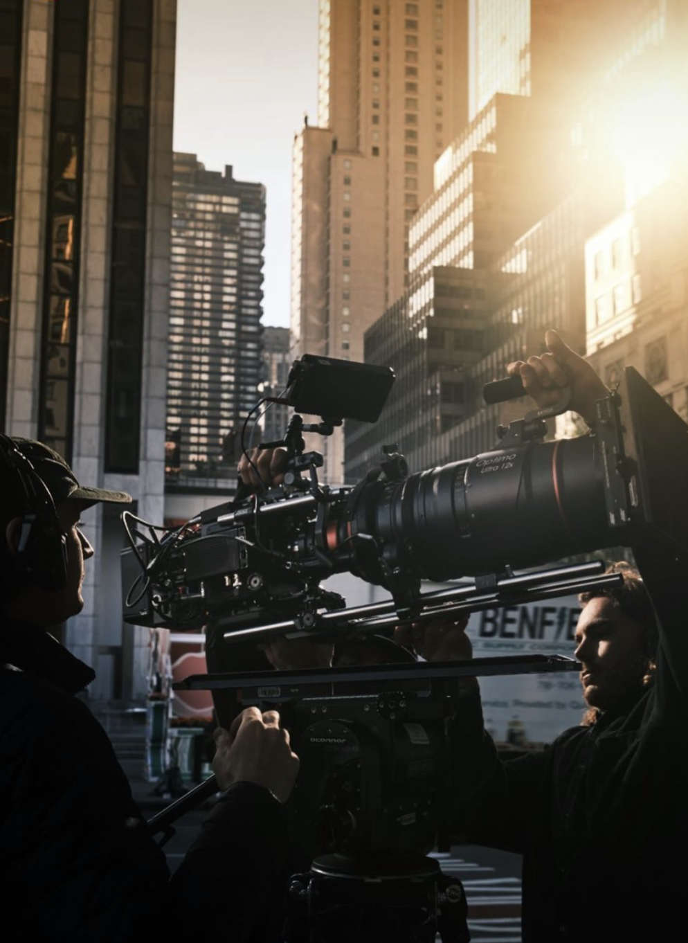 Filmmakers filming in a city street with tall skyscrapers and sunlight.