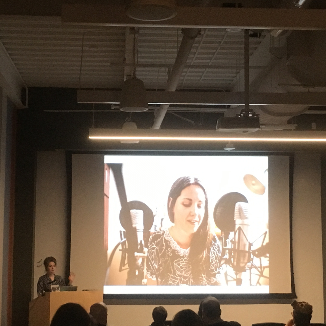 Sarah Rachel Brown lecturing in an auditorium to the Art Department at the University of Arkansas at Little Rock, sharing insights on professional practices for artists.