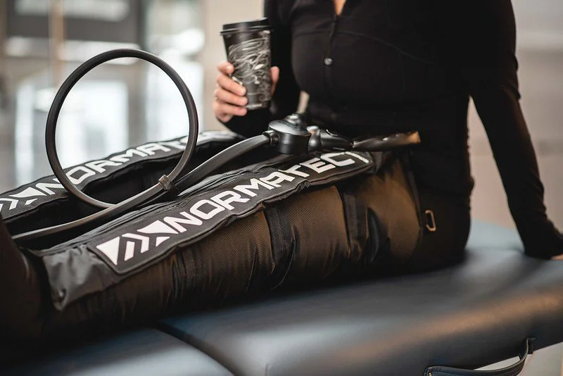 Person holding a coffee cup and sitting next to a sports bag with the brand name 'NORMATEC' on it.