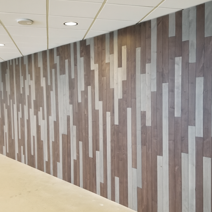 Wooden wall with alternating light and dark rectangular panels in a geometric pattern, ceiling with recessed lights.