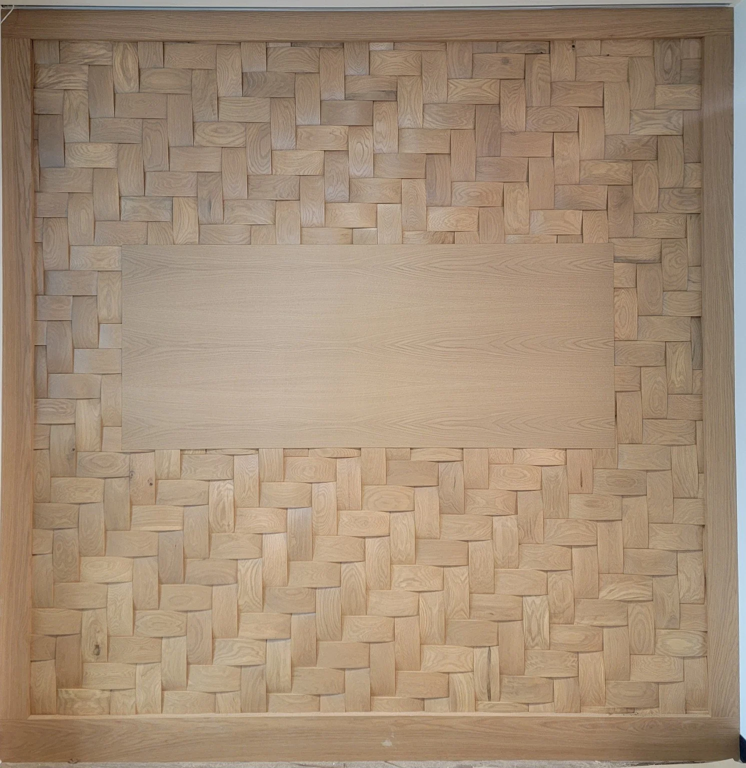 A large wall feature with a woven pattern of small square wood pieces surrounding a central solid wood panel for future signage.
