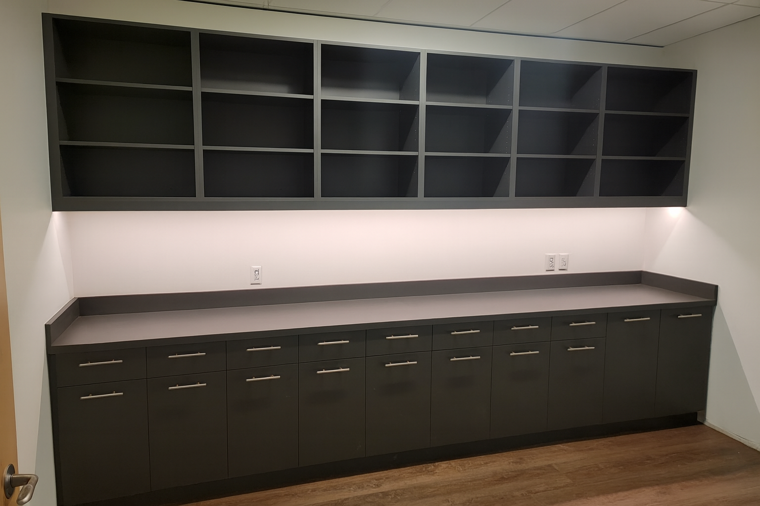 Empty black cabinets with open shelving above and drawers below, with a white wall behind and electrical outlets.