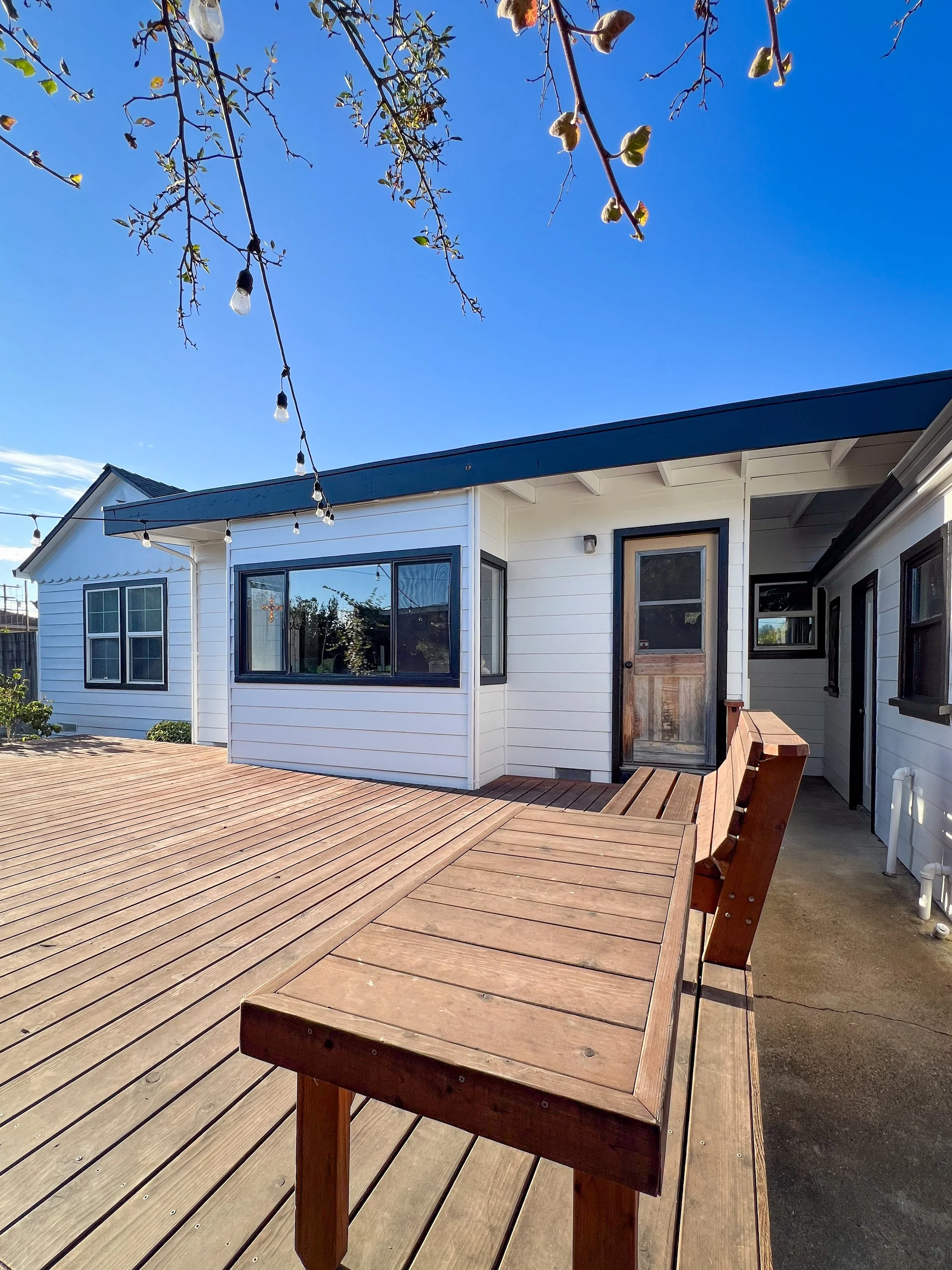 Photo of a backyard deck with a house in the background, string lights hanging from a tree, and a clear blue sky.