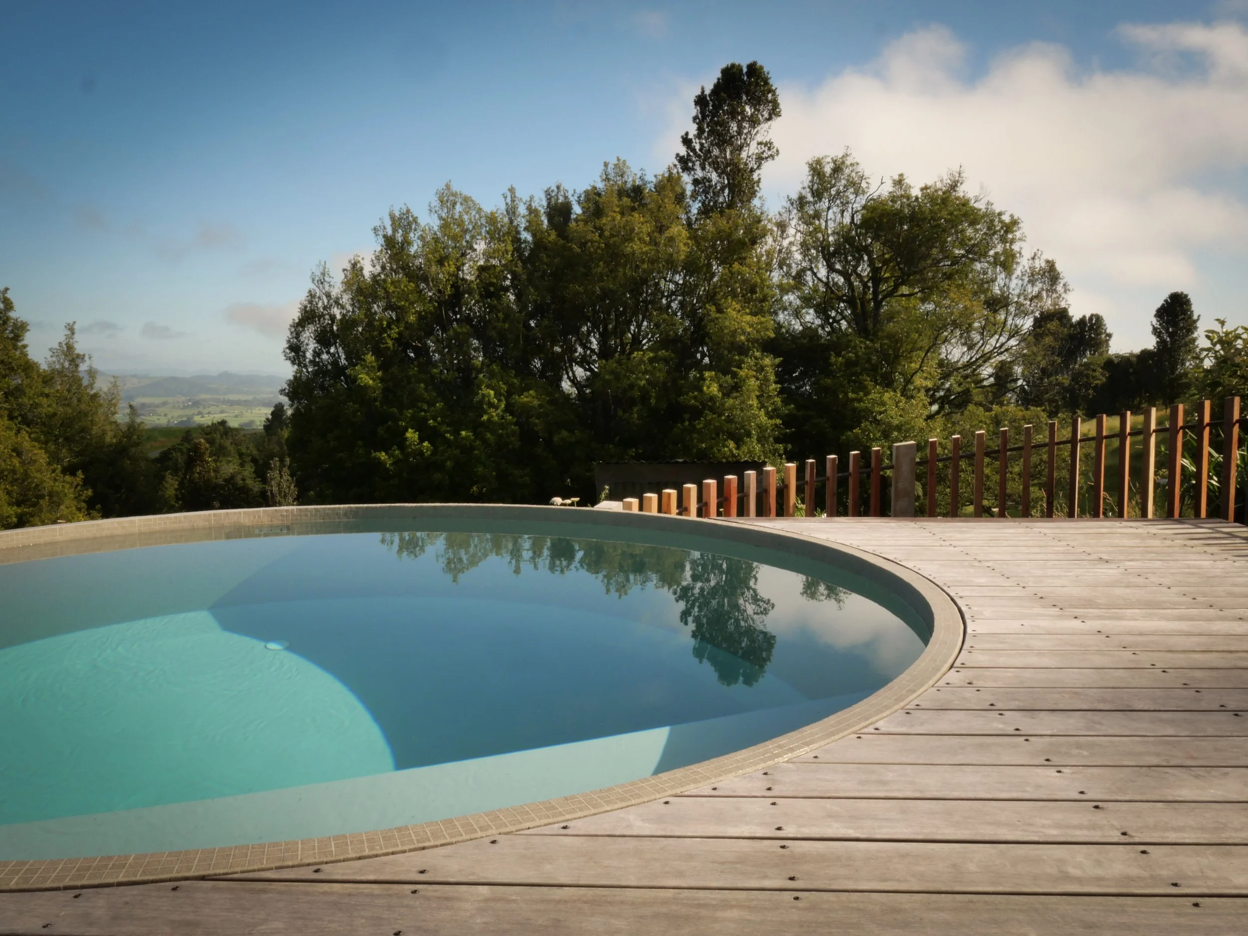 A concrete water tank  small swimming pool, framed by Australian recycled hardwood decking with bespoke copper pipe and hardwood batten fence overlooking the Waikato