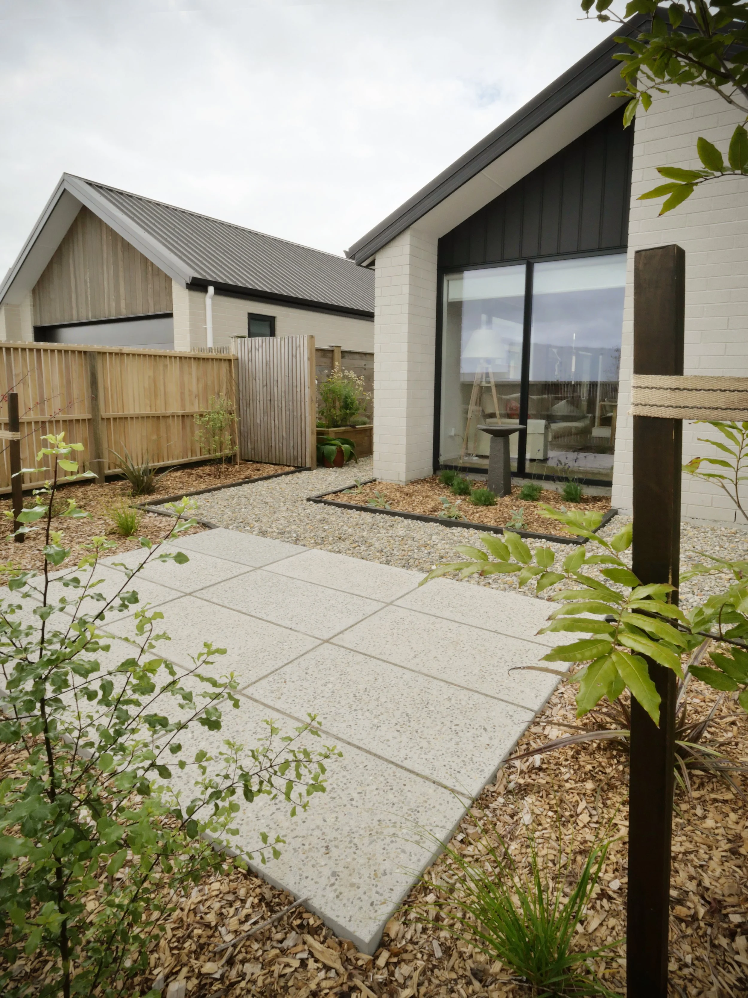A modern house with large glass windows, a white brick exterior, and a garden with gravel and plants in the backyard.