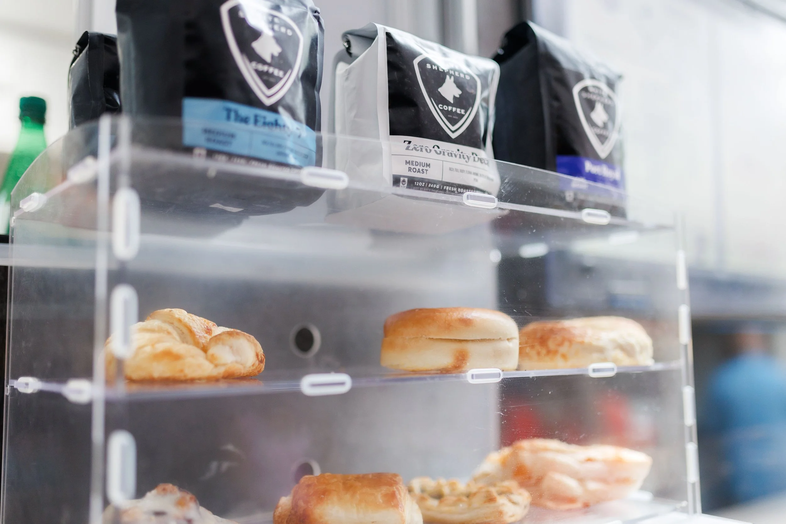Display case with assorted baked goods and bags of coffee on top, in a coffee shop or bakery setting.
