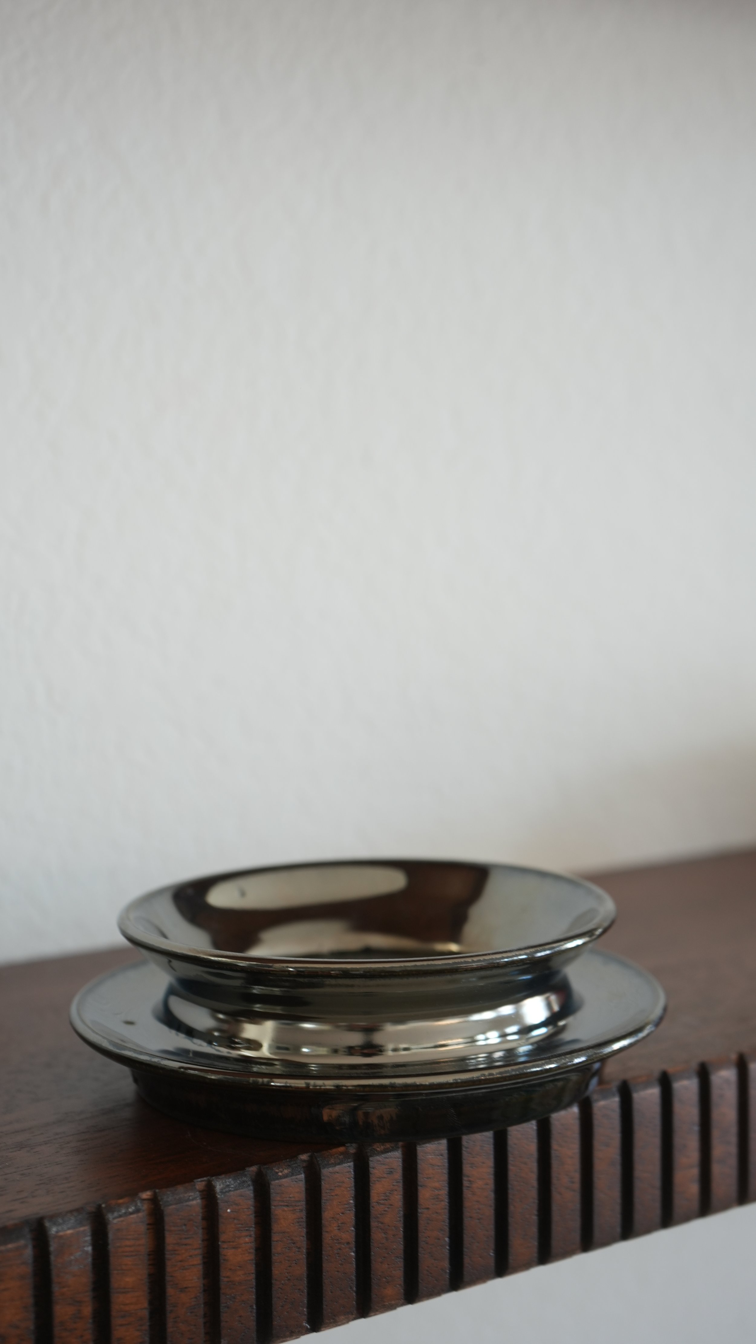 A set of three stacked reflecting metallic bowls on a wooden surface, with a white wall in the background.