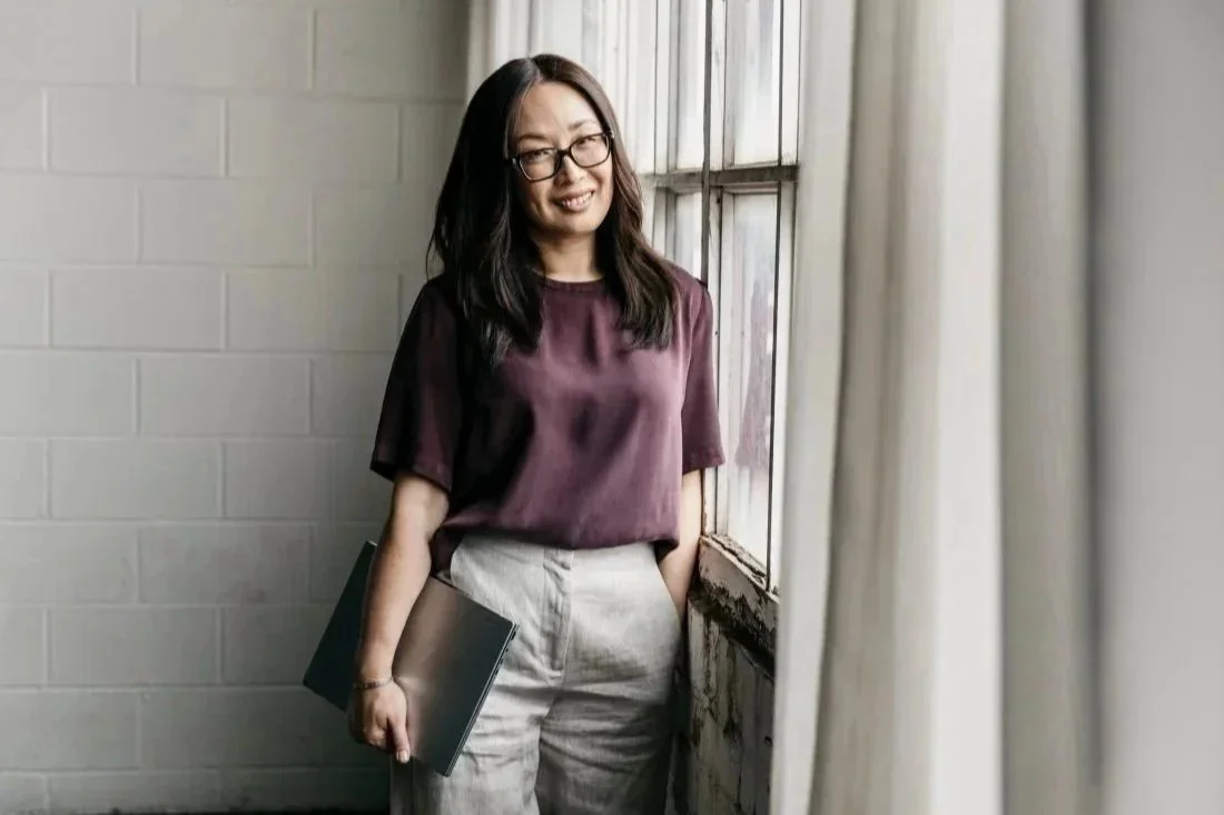 Person standing by a window holding a laptop