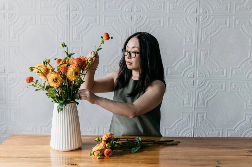 Person arranging flowers in a vase on a table