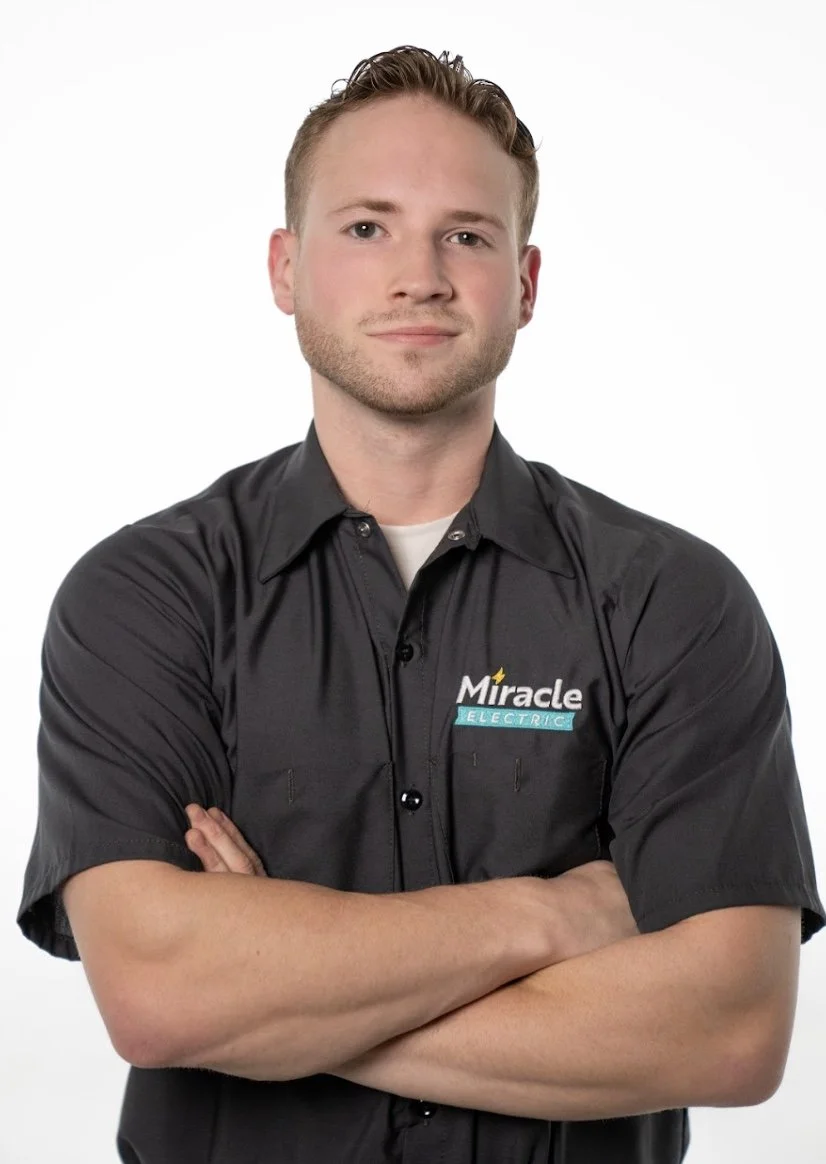 Two men standing outdoors near a house, giving thumbs up. One is young with short blonde hair, wearing a blue shirt and beige pants. The other has a long white beard, sunglasses, a black Harley Davidson t-shirt, and camouflage shorts; he is holding an umbrella over his head.