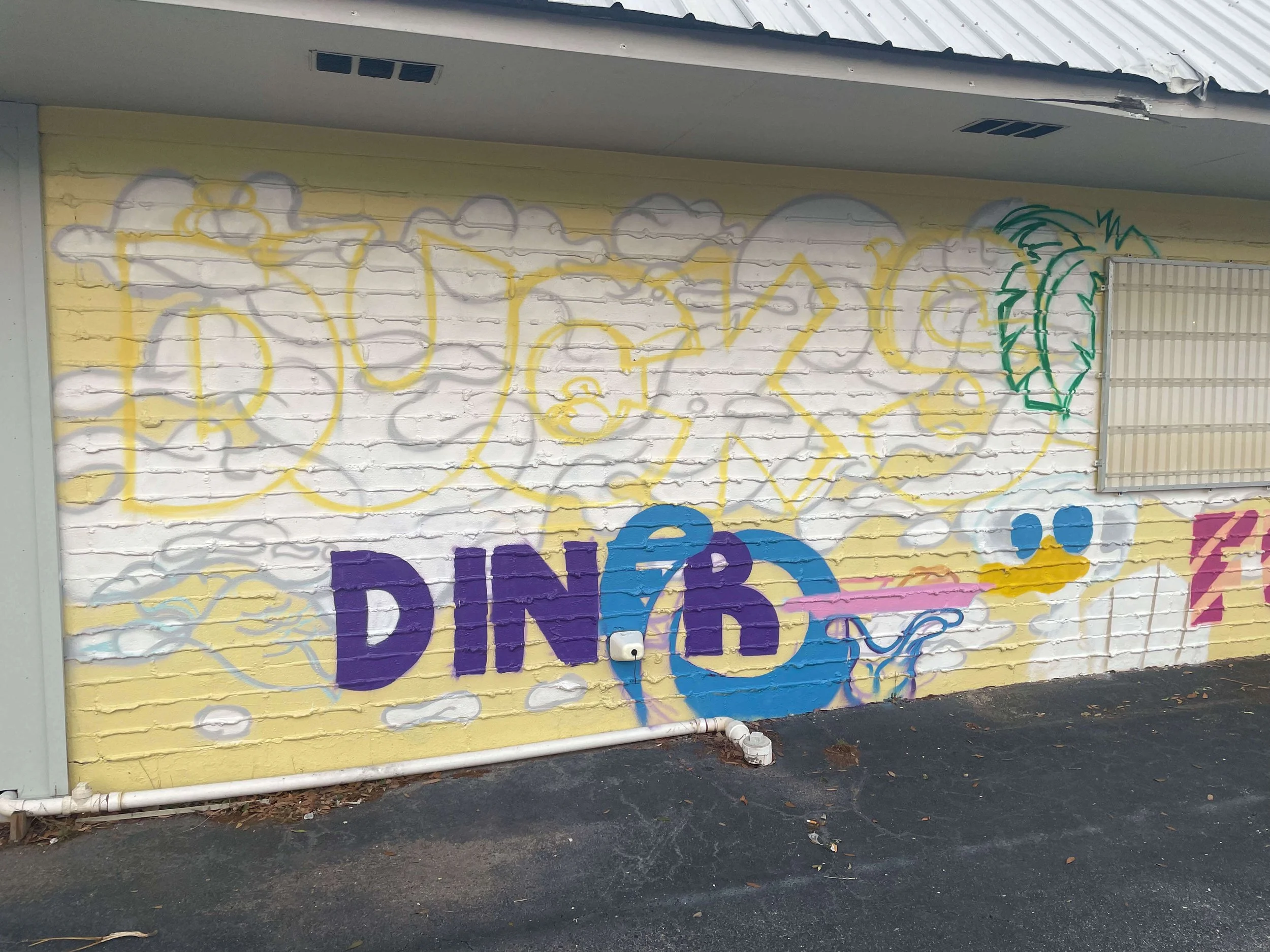 Progress photo of Duck’s Diner mural in Gulf Shores, Alabama, featuring the large red and yellow “Duck’s” lettering partially completed against the bright yellow background, 2025.