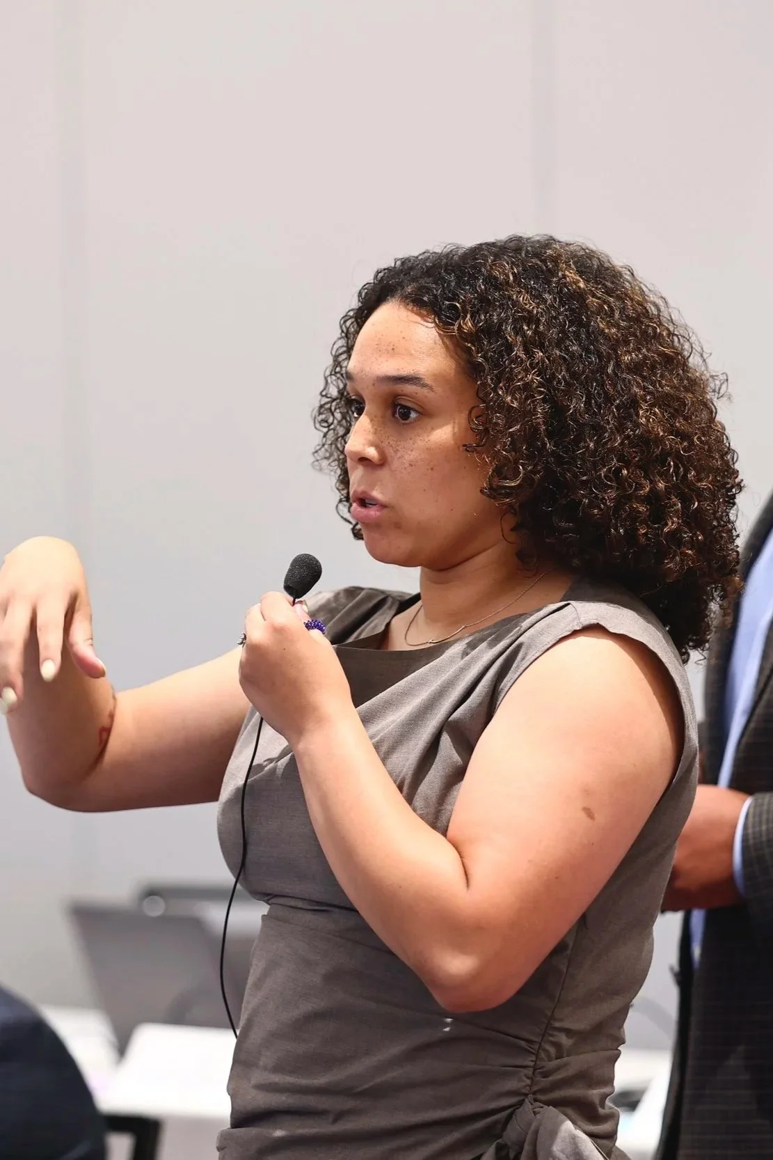 A woman with curly hair speaking into a microphone during a meeting or presentation.