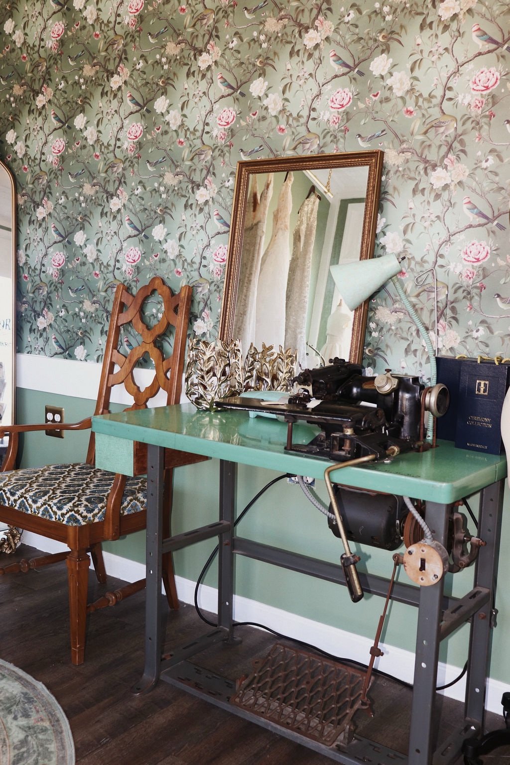 Vintage sewing machine close-up on a green desk, mirror reflecting gowns