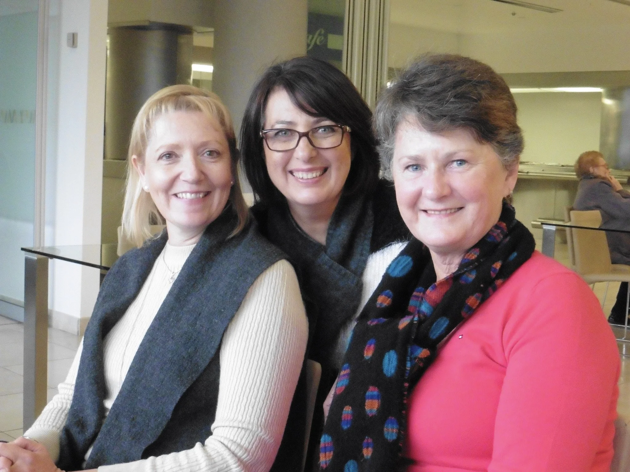 Three smiling women sitting close together indoors, posing for the photo.