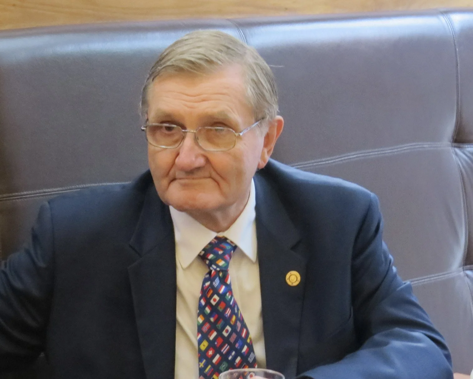 Man in a dark suit and colourful patterned tie sitting at a restaurant table with a brown leather booth behind him.