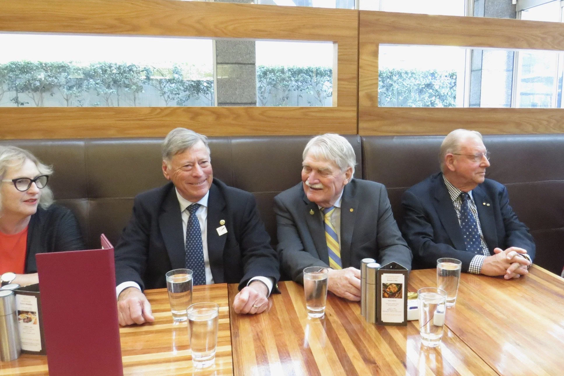 Four older adults seated at a restaurant booth, engaged in conversation, with drinks and menus on the table.
